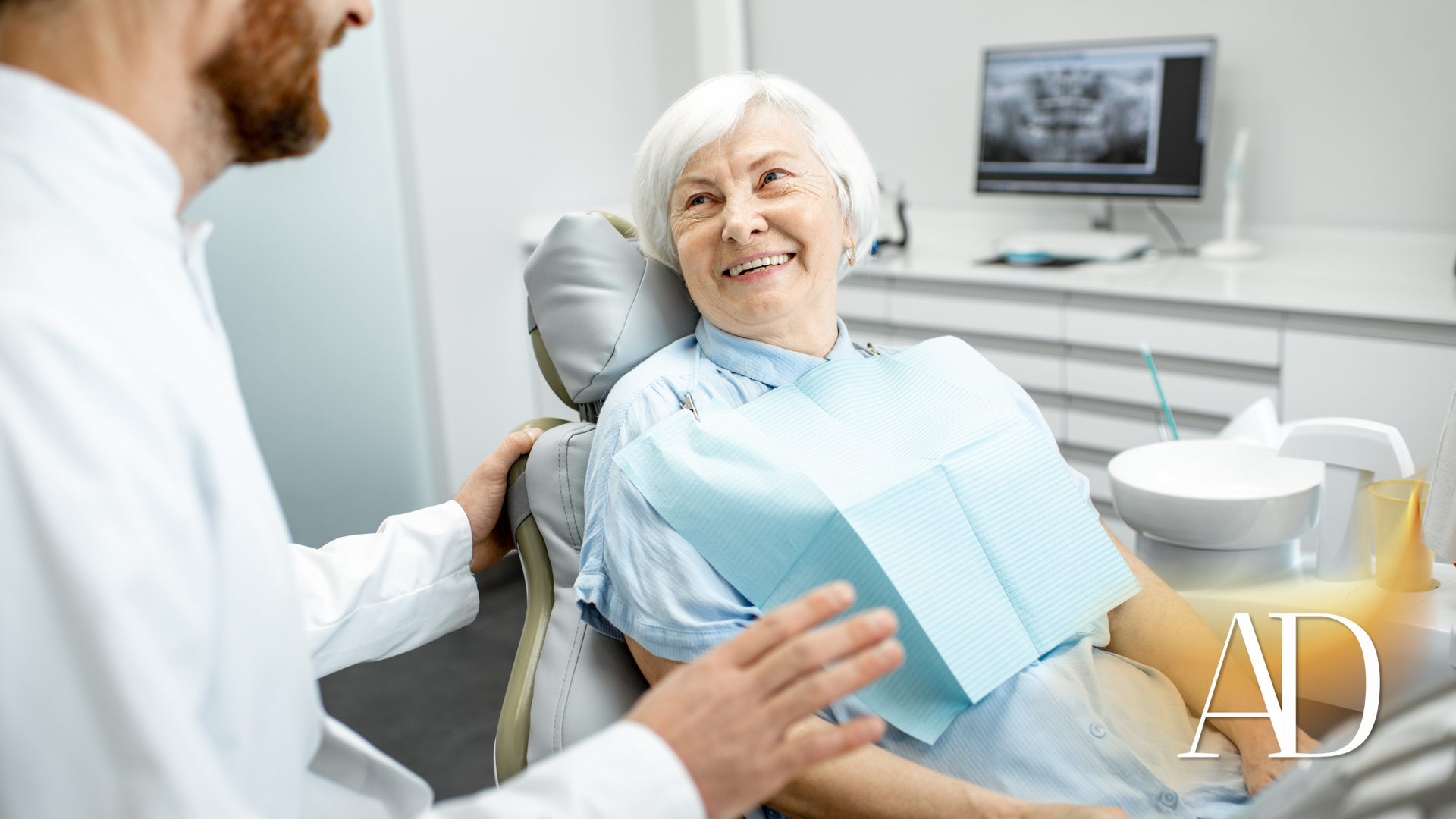 Smiling patient in a dental chair as a dentist speaks to her in a bright clinic