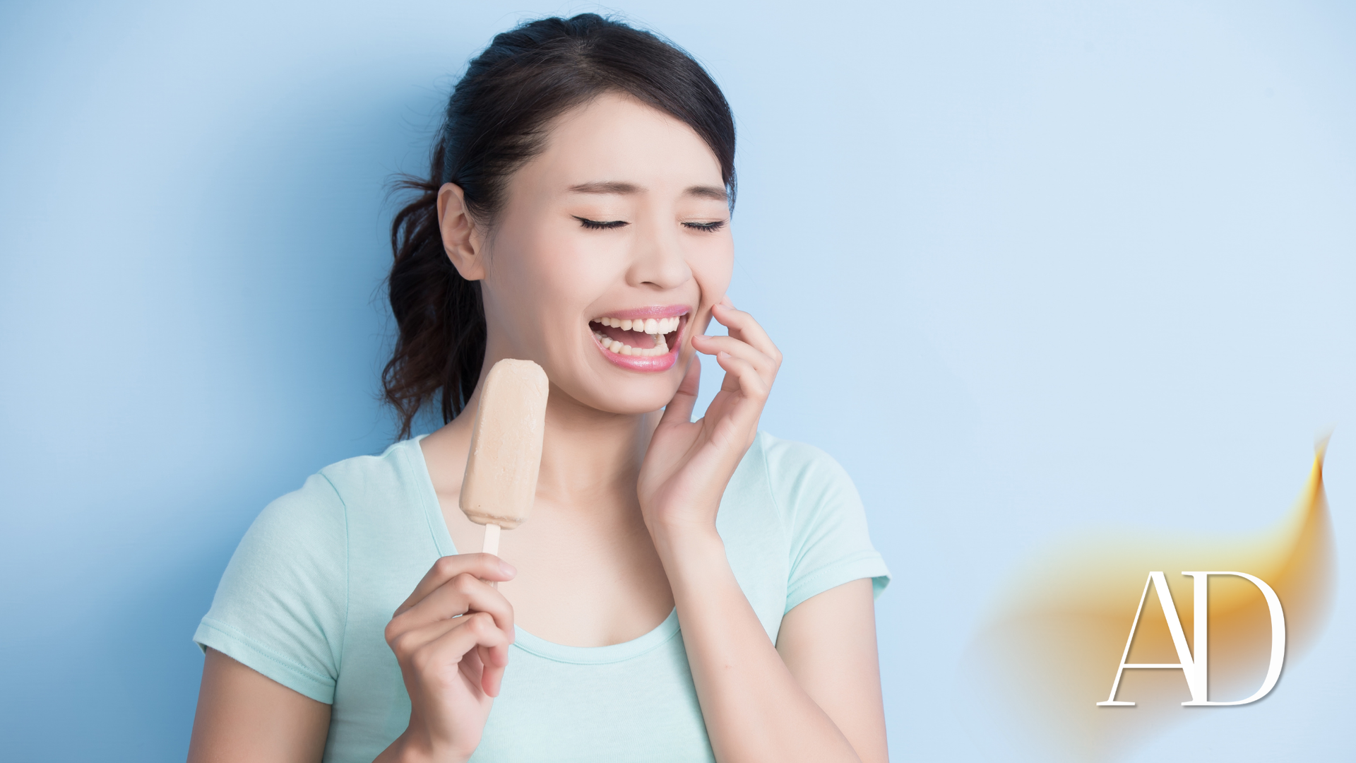 Smiling woman holding an ice cream bar against a light blue background