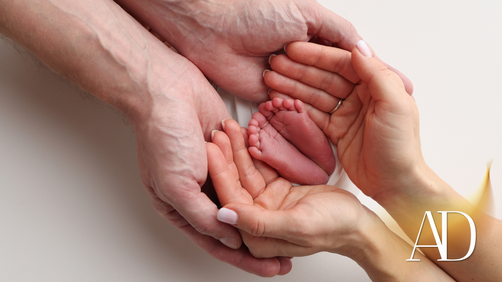 Adult and child hands cradling a baby’s feet in a soft, close-up family scene