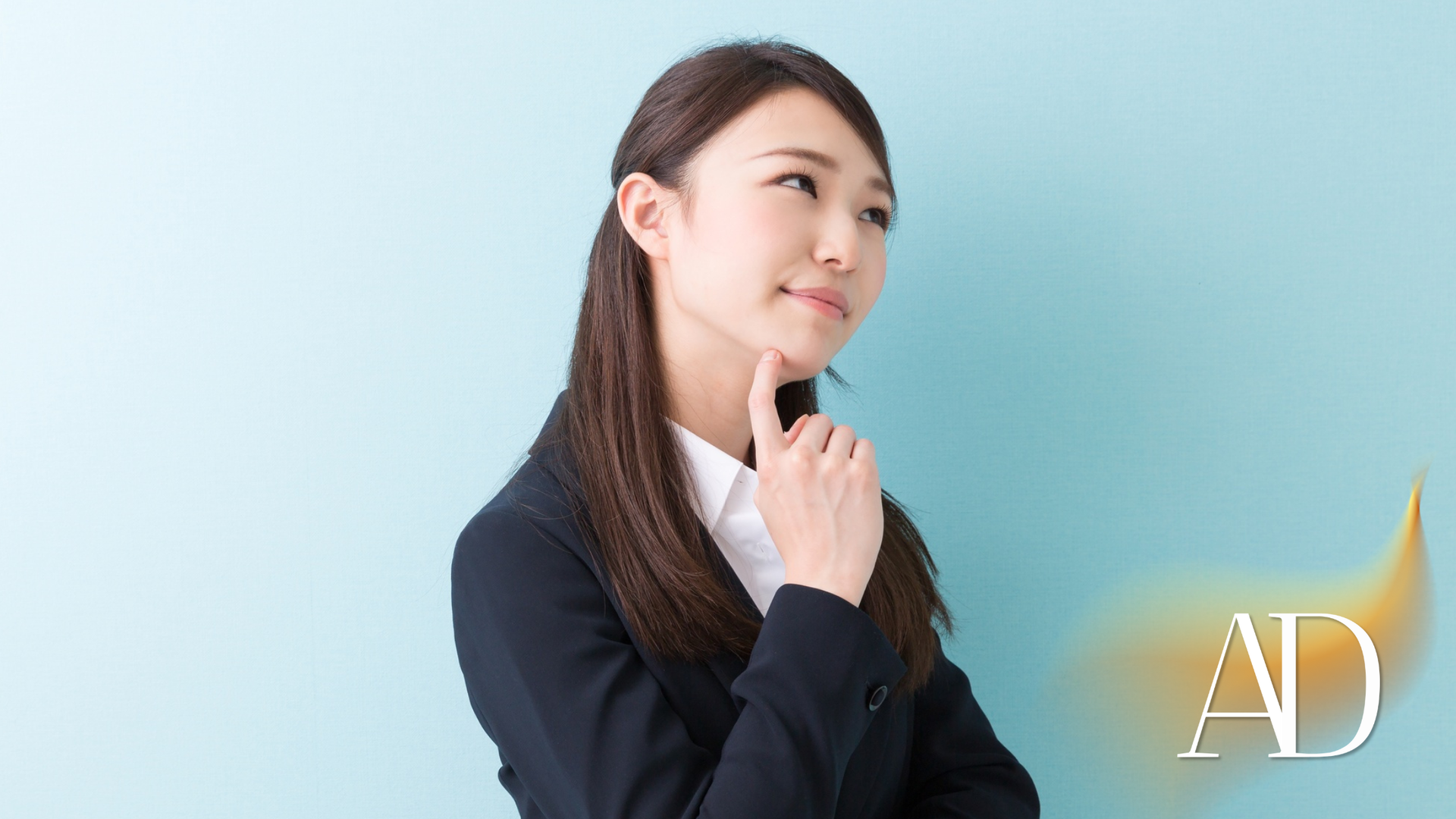 Thoughtful person in a dark blazer against a light blue background, hand on chin.
