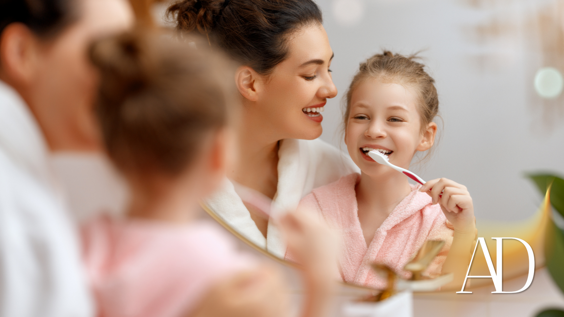 Mother and daughter smiling while brushing teeth together in a bright bathroom