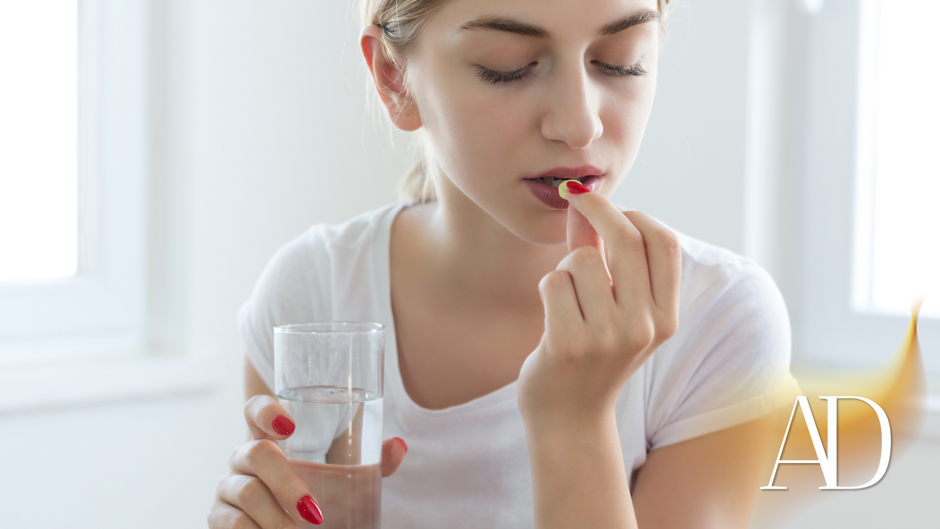 Woman taking a pill with a glass of water in a bright room