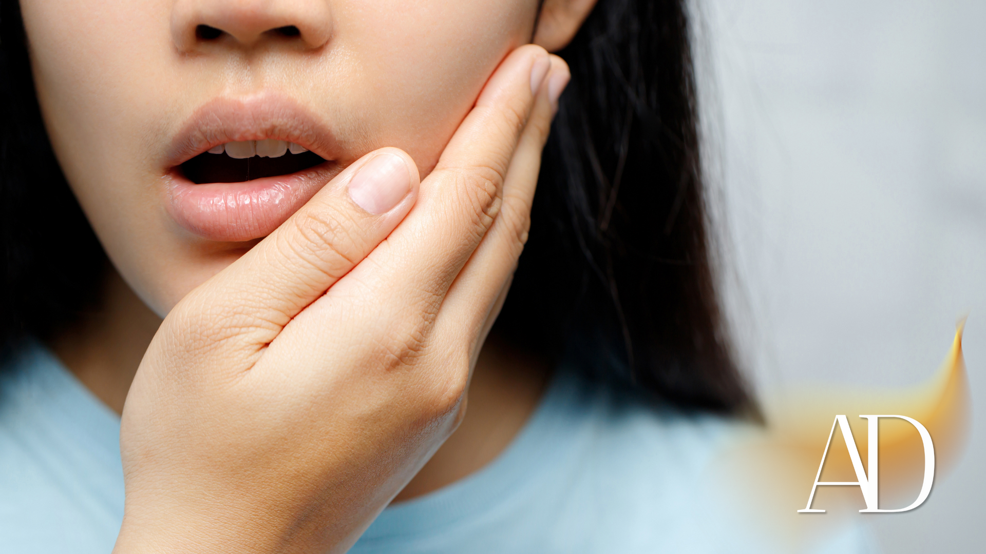 Person touching cheek near mouth, lips slightly open, with “AD” watermark in the corner.
