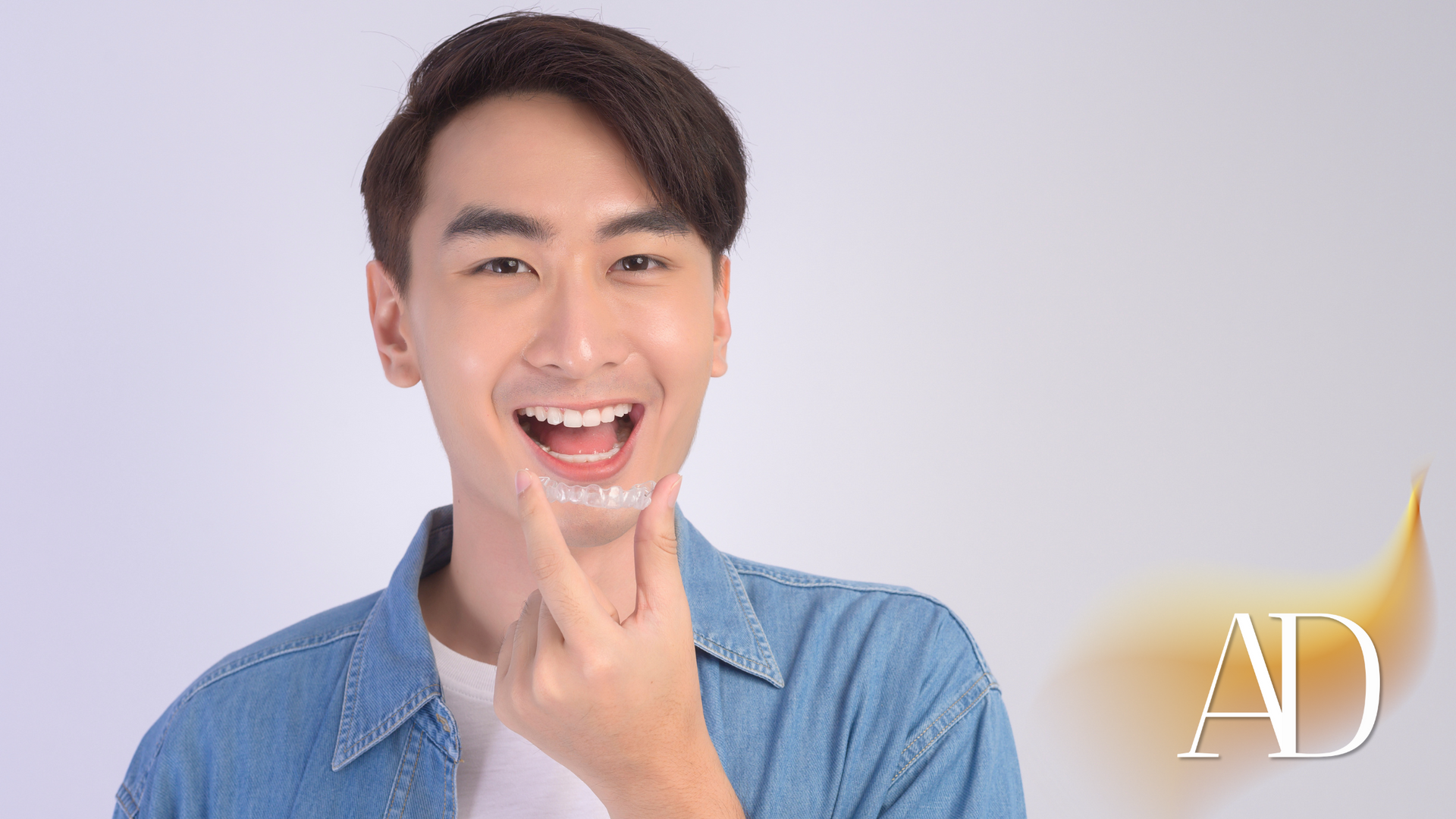 Smiling man in a denim shirt touching his chin against a light gray background