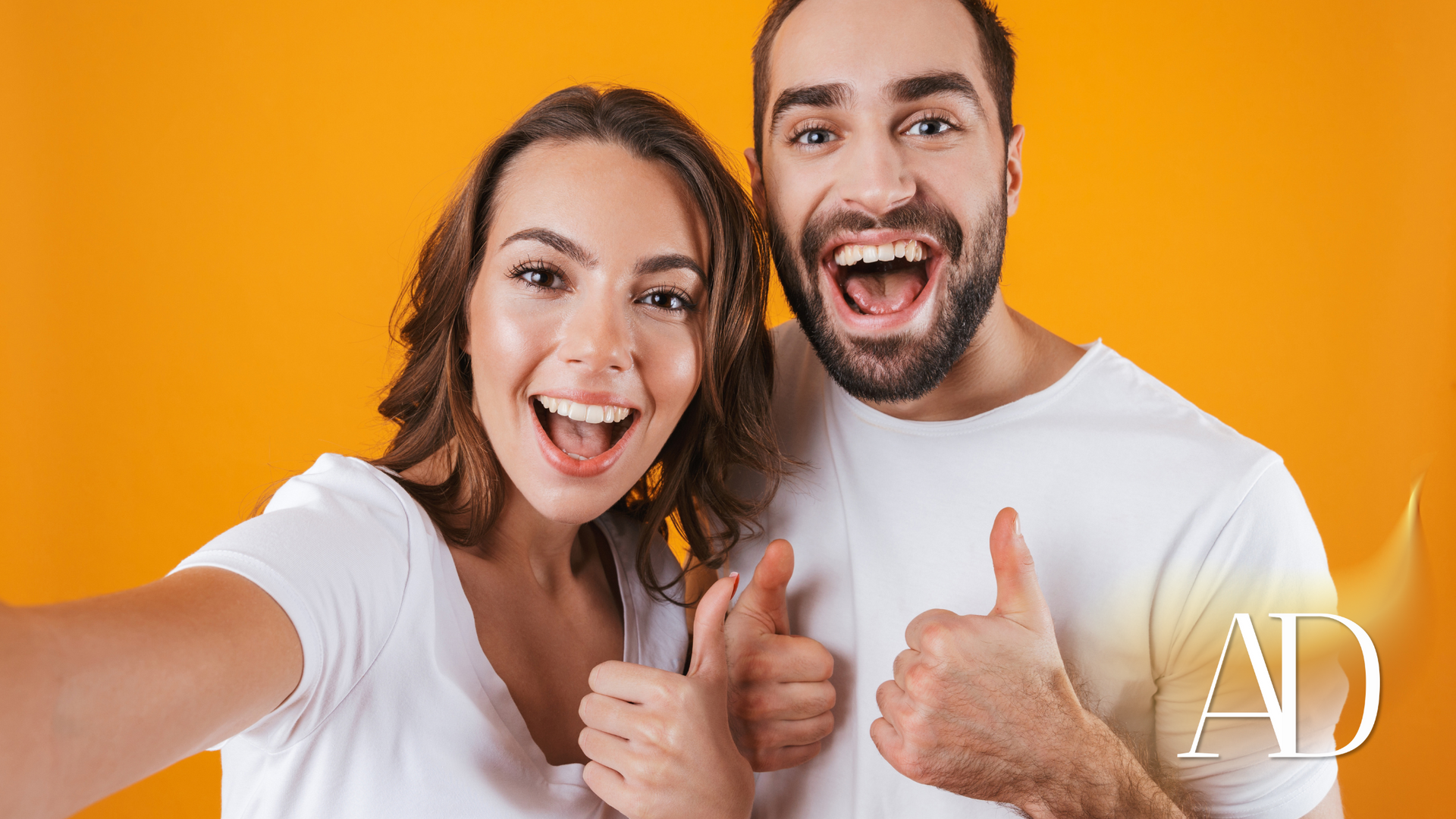 Two smiling people taking a selfie and giving thumbs up against a bright orange background