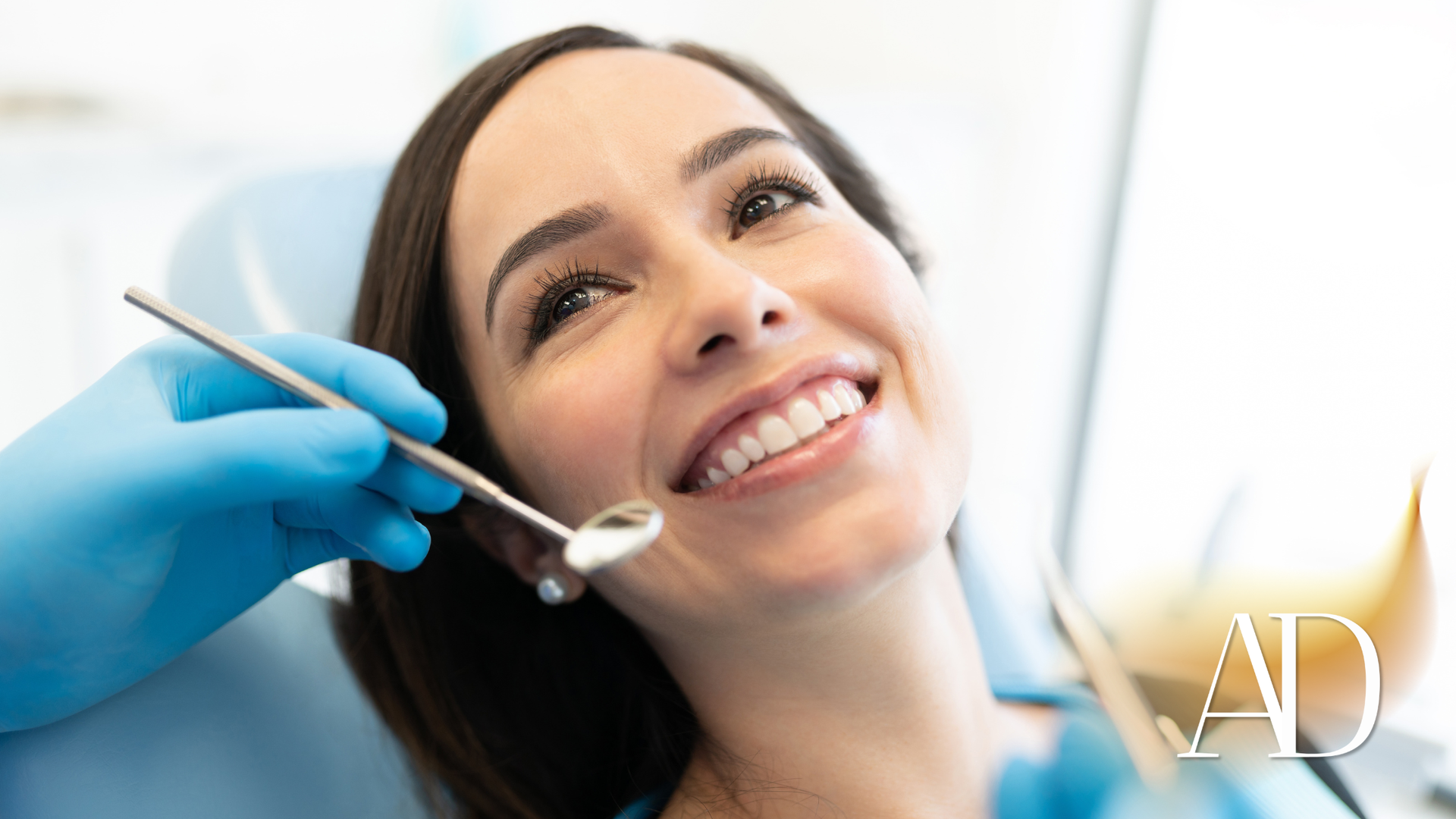 Dentist using a mirror and tool to examine a smiling patient in a bright clinic