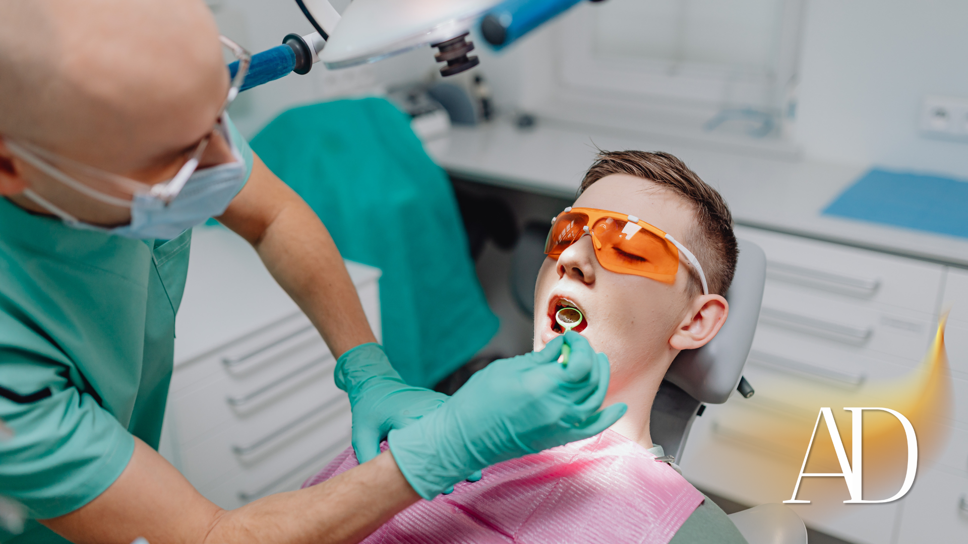 Dentist examining a patient in a dental chair, wearing orange eye shields and pink bib