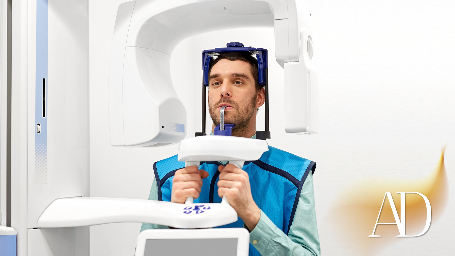 Man in blue vest using dental scanner in a white clinic room