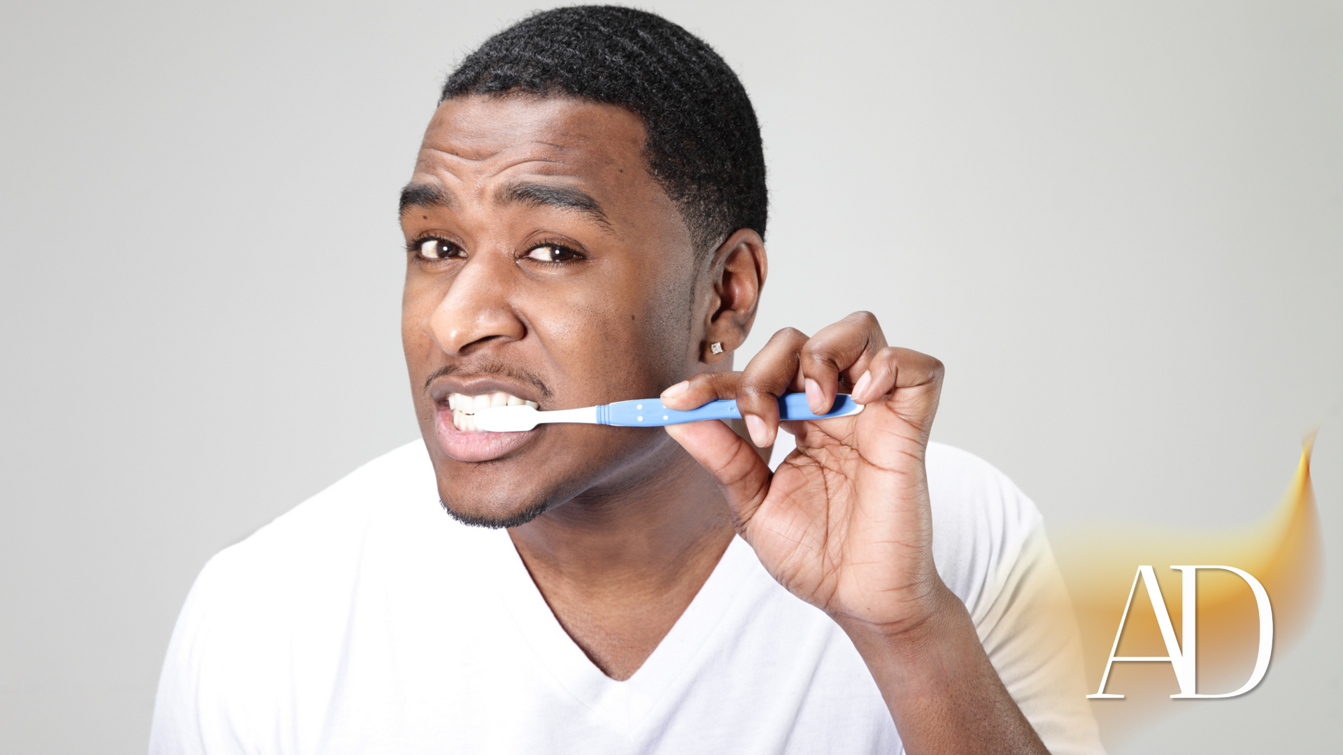 Man brushing teeth with a blue toothbrush and smiling in a bright studio setting