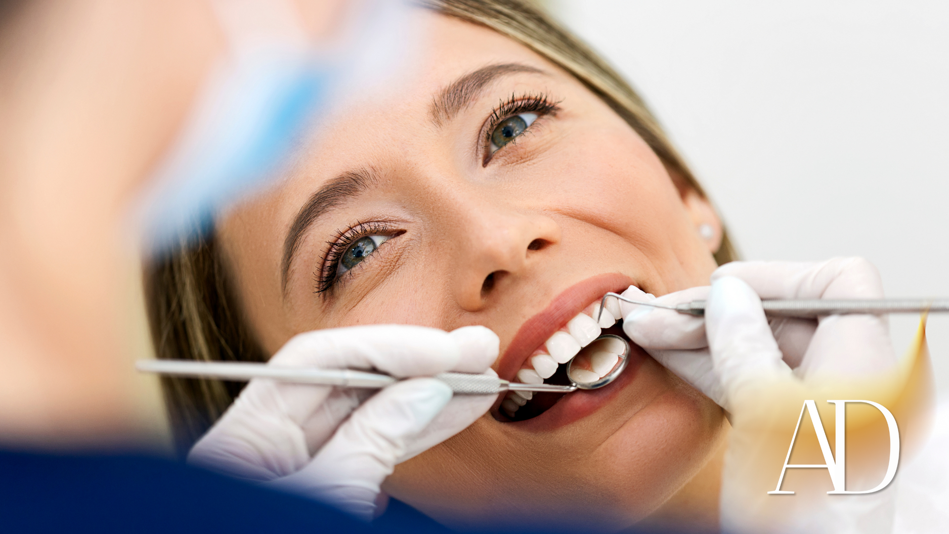 Dentist examining a smiling patient’s teeth with dental tools in a clinic