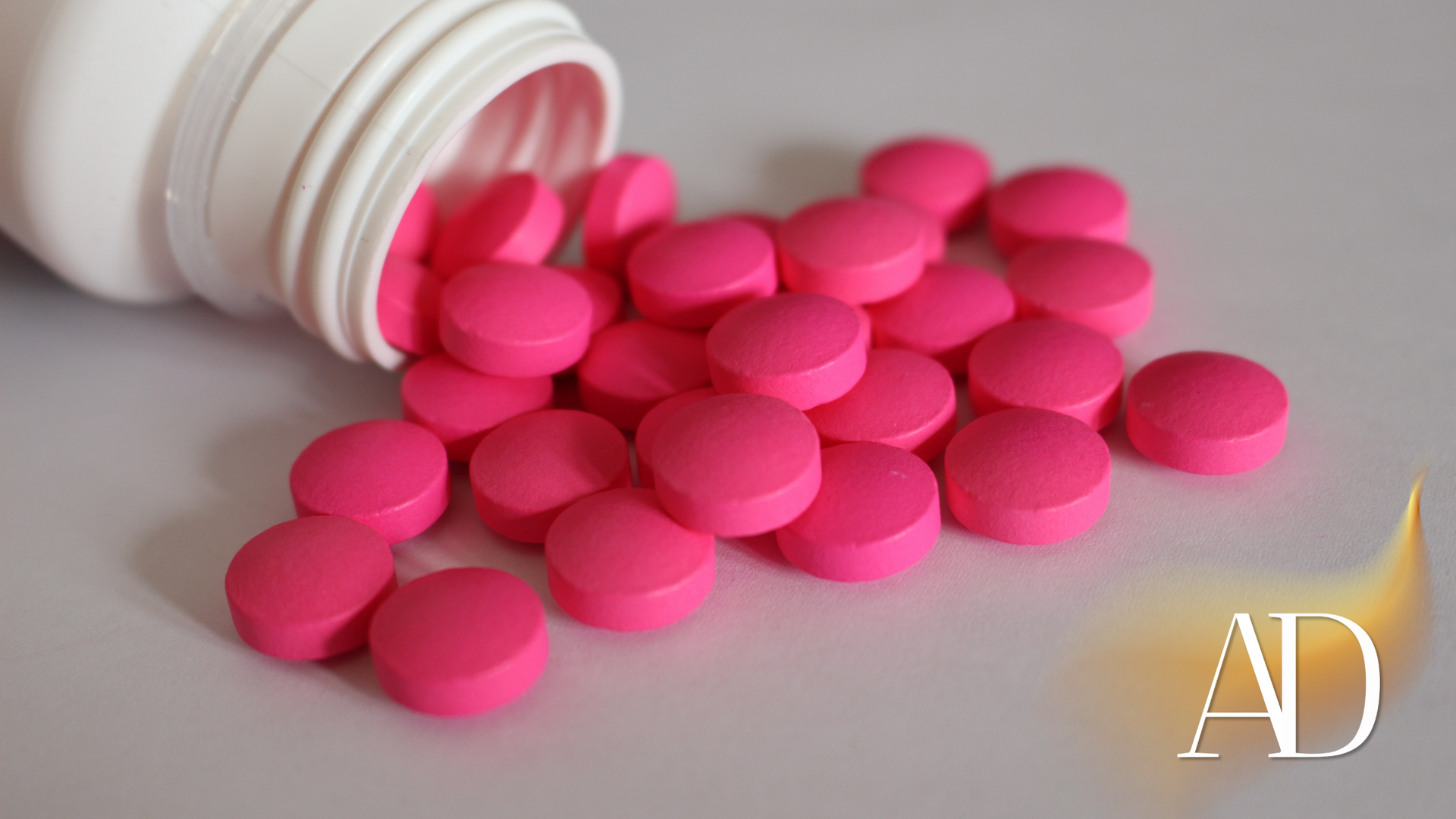Pink pills spilling from a white pill bottle on a light surface