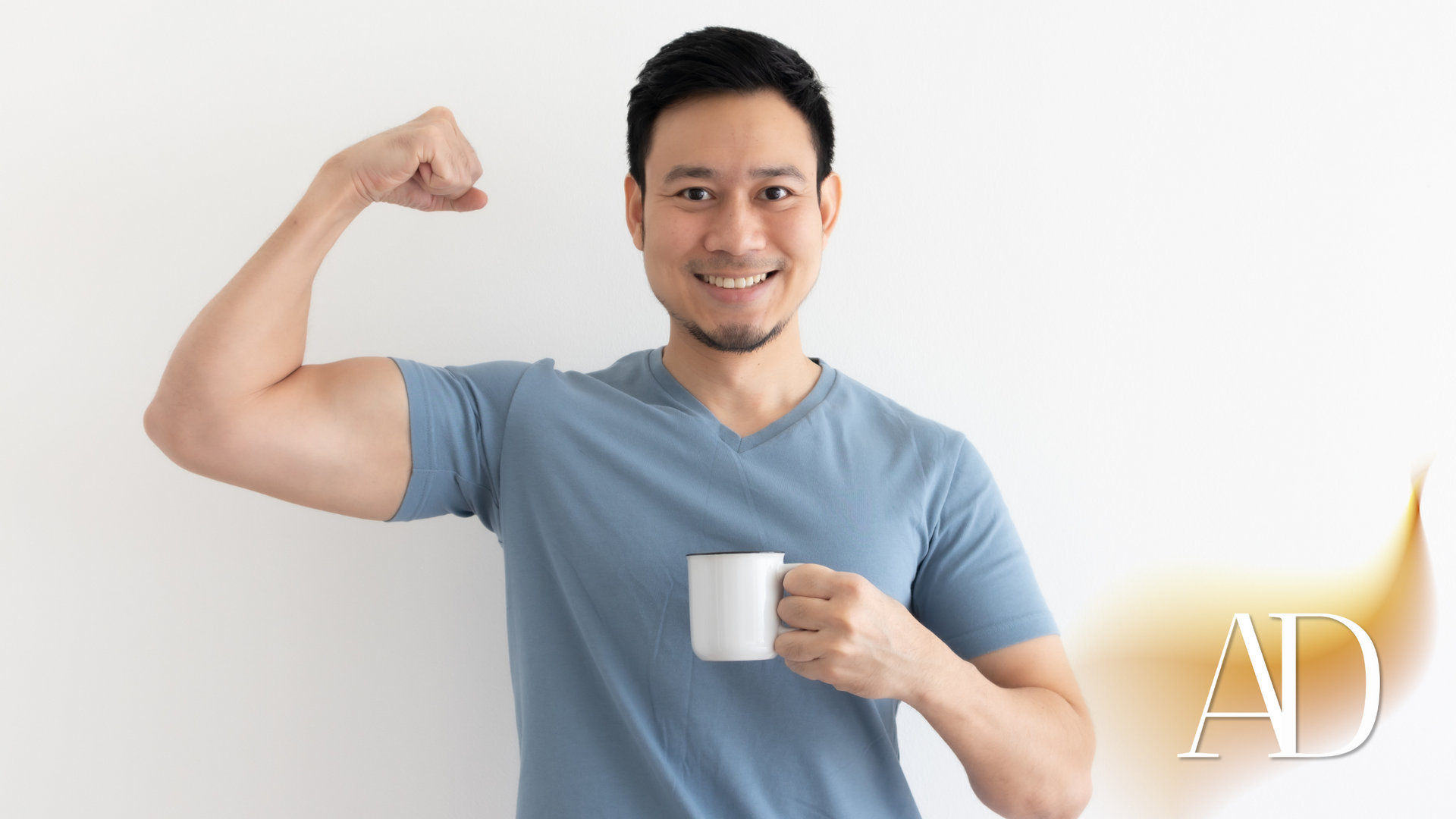 Smiling man in blue shirt flexing his arm while holding a white mug against a light background