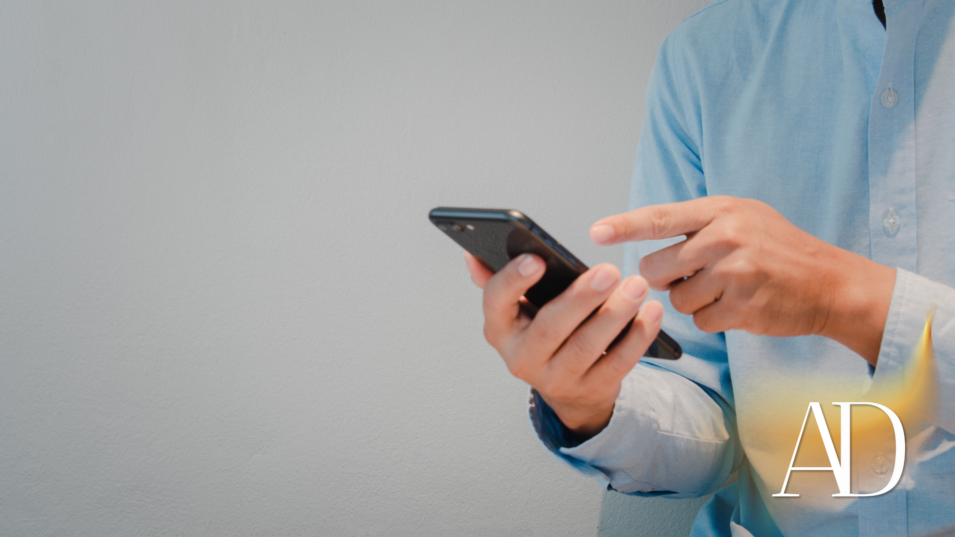 Person in a light blue shirt using a smartphone and pointing at the screen, with an AD logo in the corner