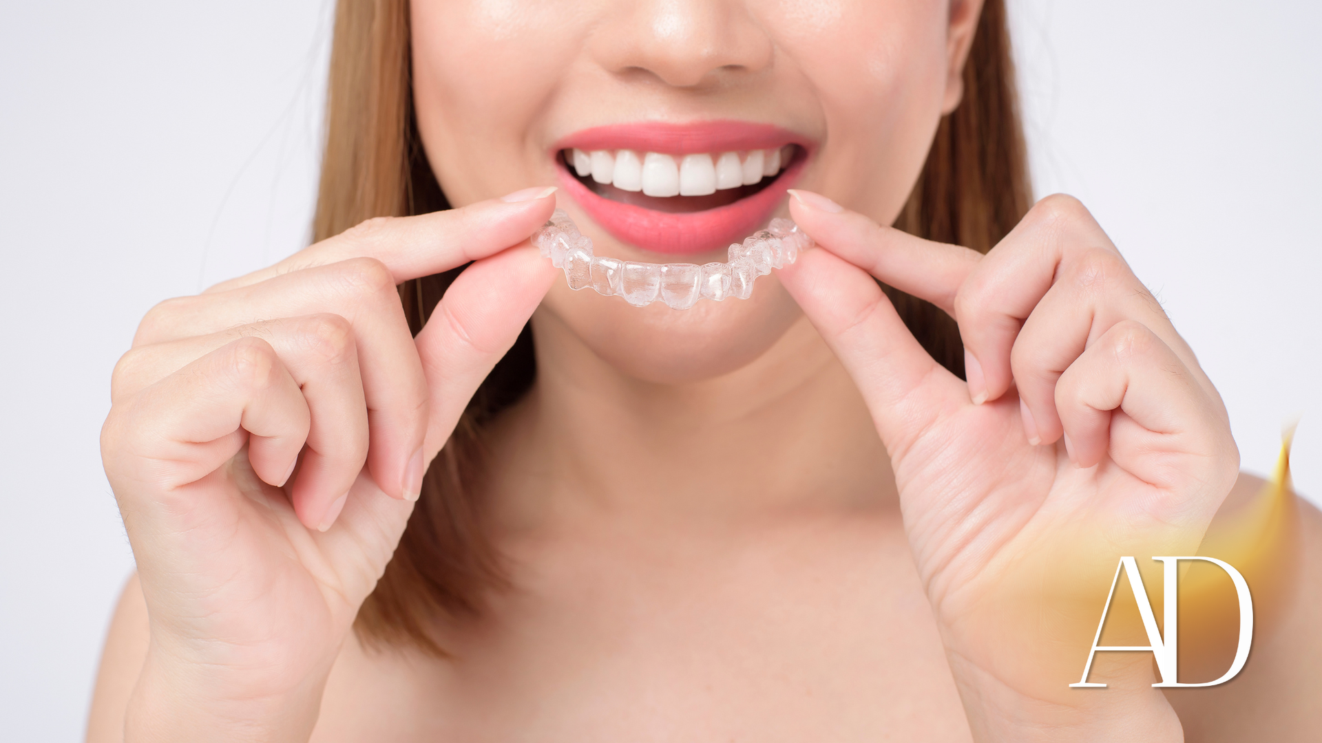 Woman smiling while inserting clear aligners onto her teeth