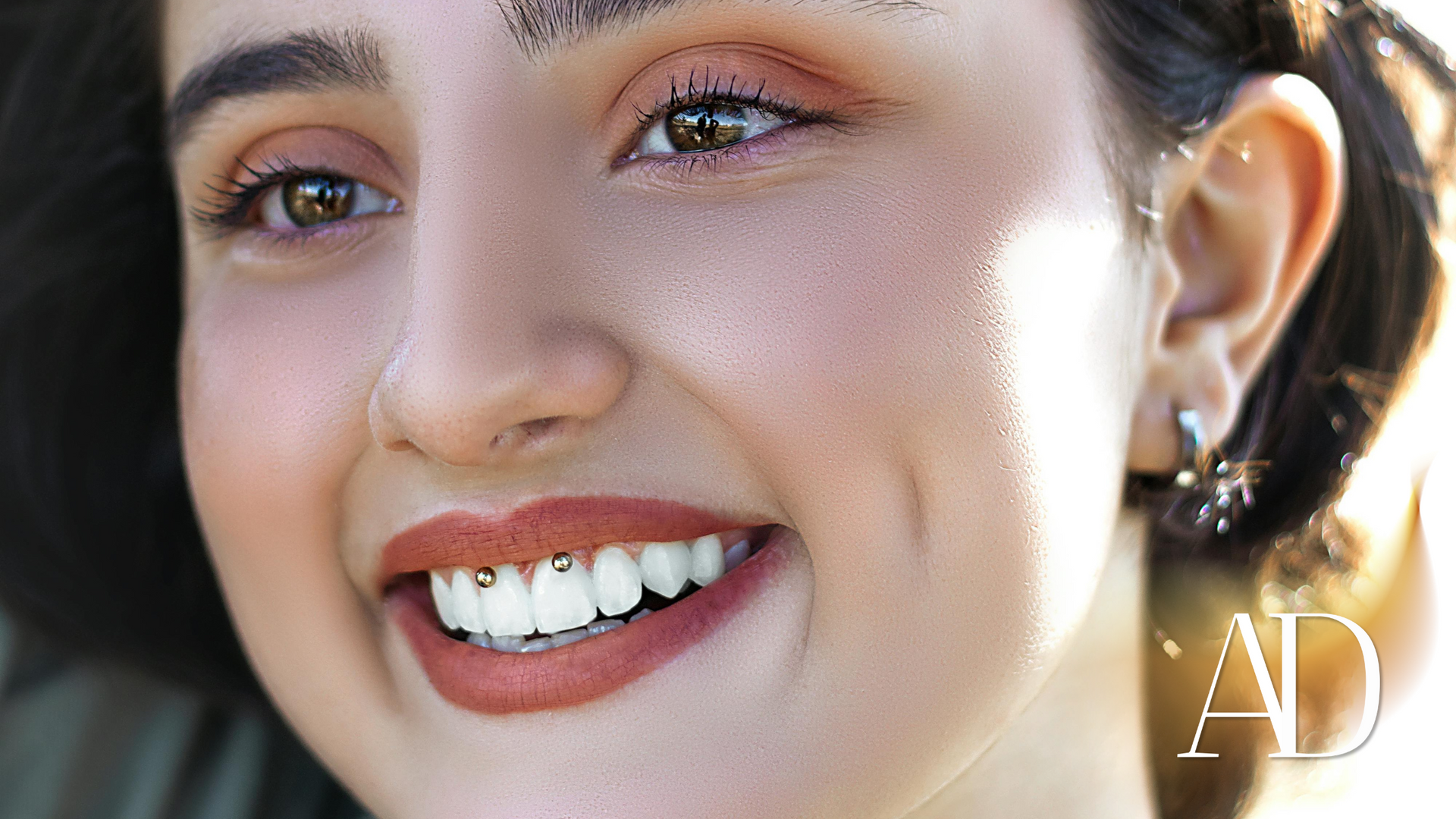 Smiling woman’s face close-up with glossy makeup and an earring against a blurred background.