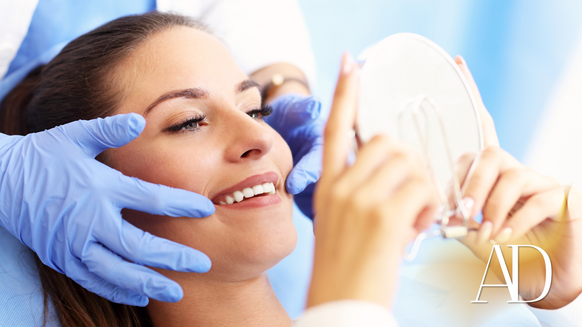 Gloved hands applying facial treatment to a smiling woman holding a mirror