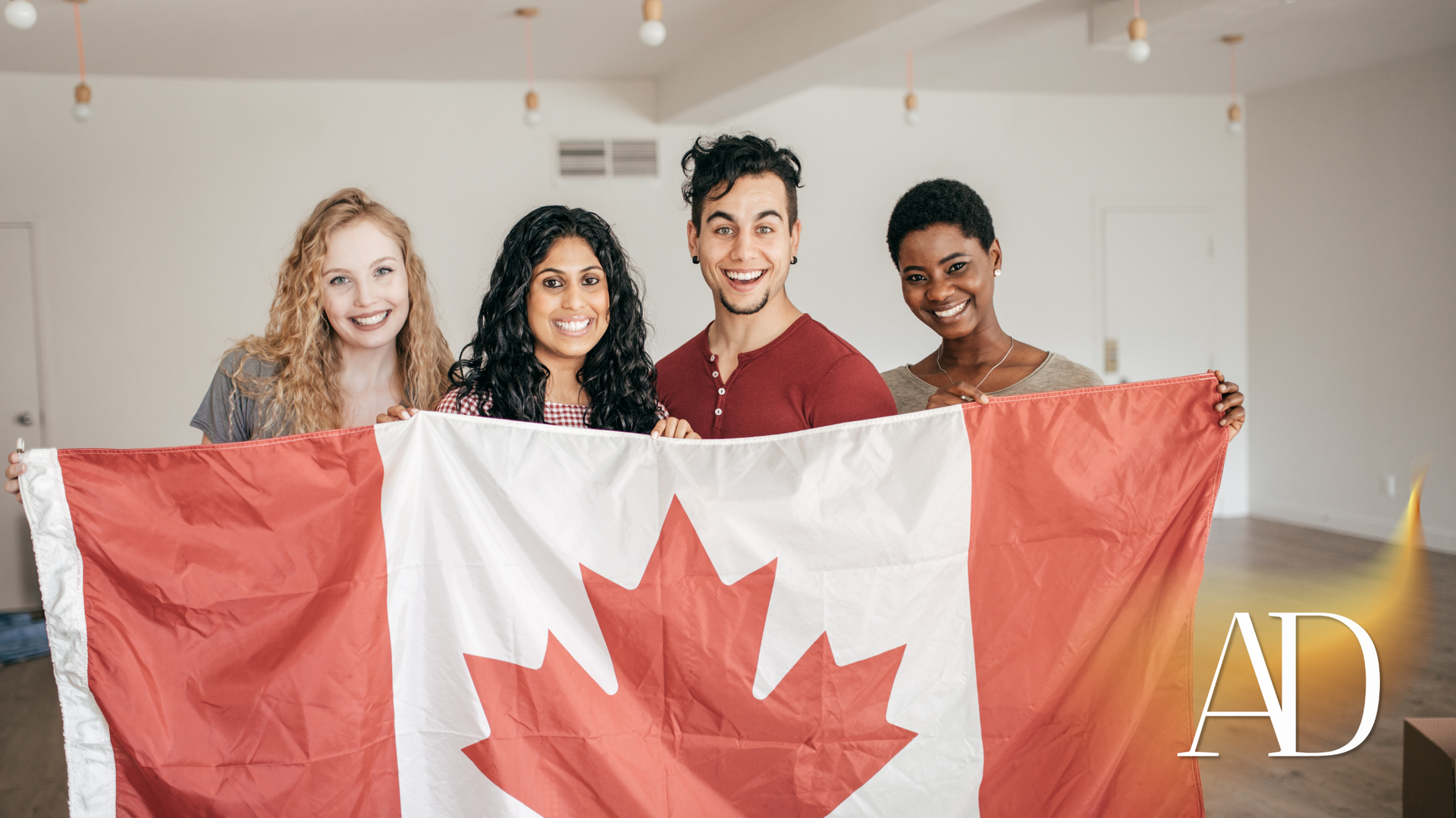 Four people smiling and holding a Canadian flag indoors.