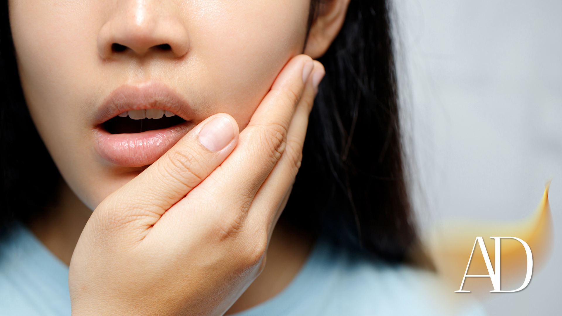 Close-up of a person holding their cheek with parted lips, suggesting tooth or jaw pain.
