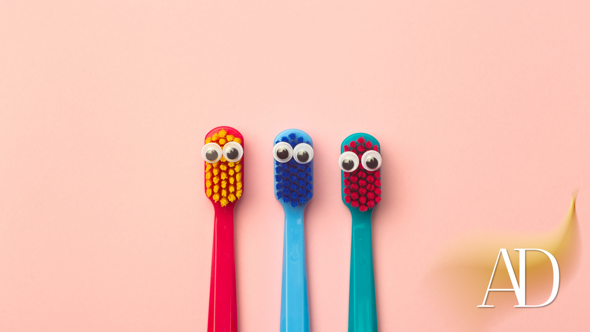 Three colorful toothbrushes with googly eyes against a pink background
