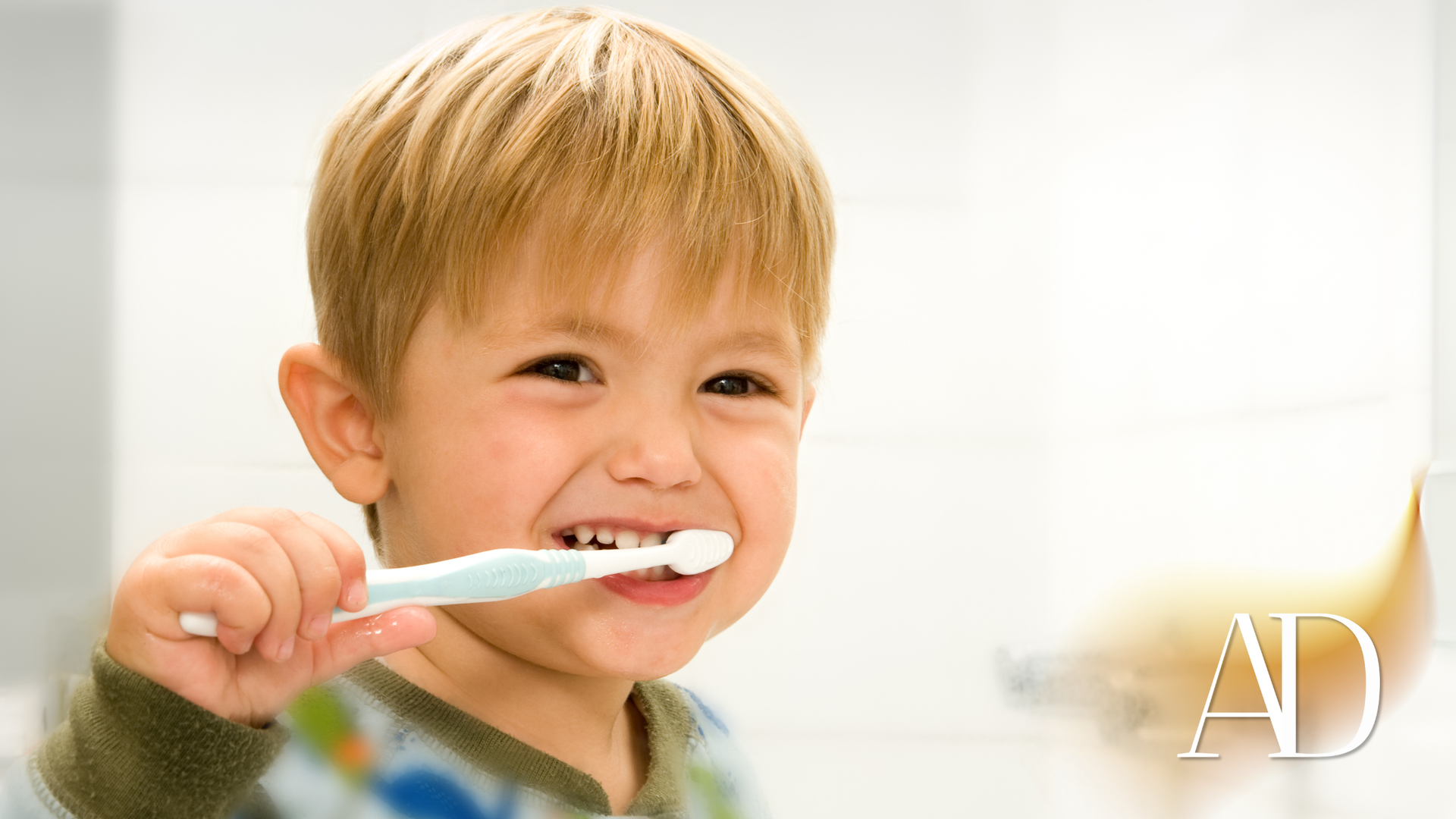 Child brushing teeth in a bright bathroom, smiling and holding a toothbrush.