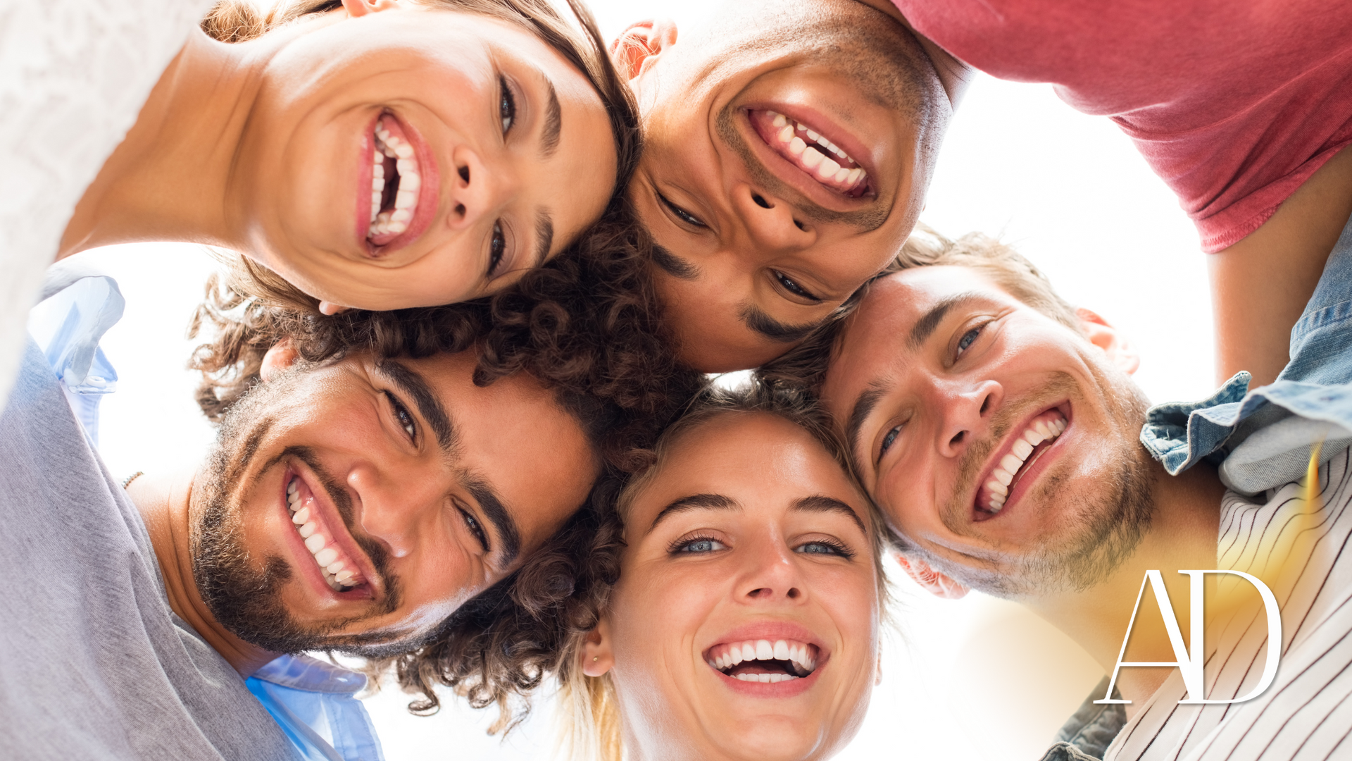 Six smiling friends circle the camera outdoors against a bright blue sky.