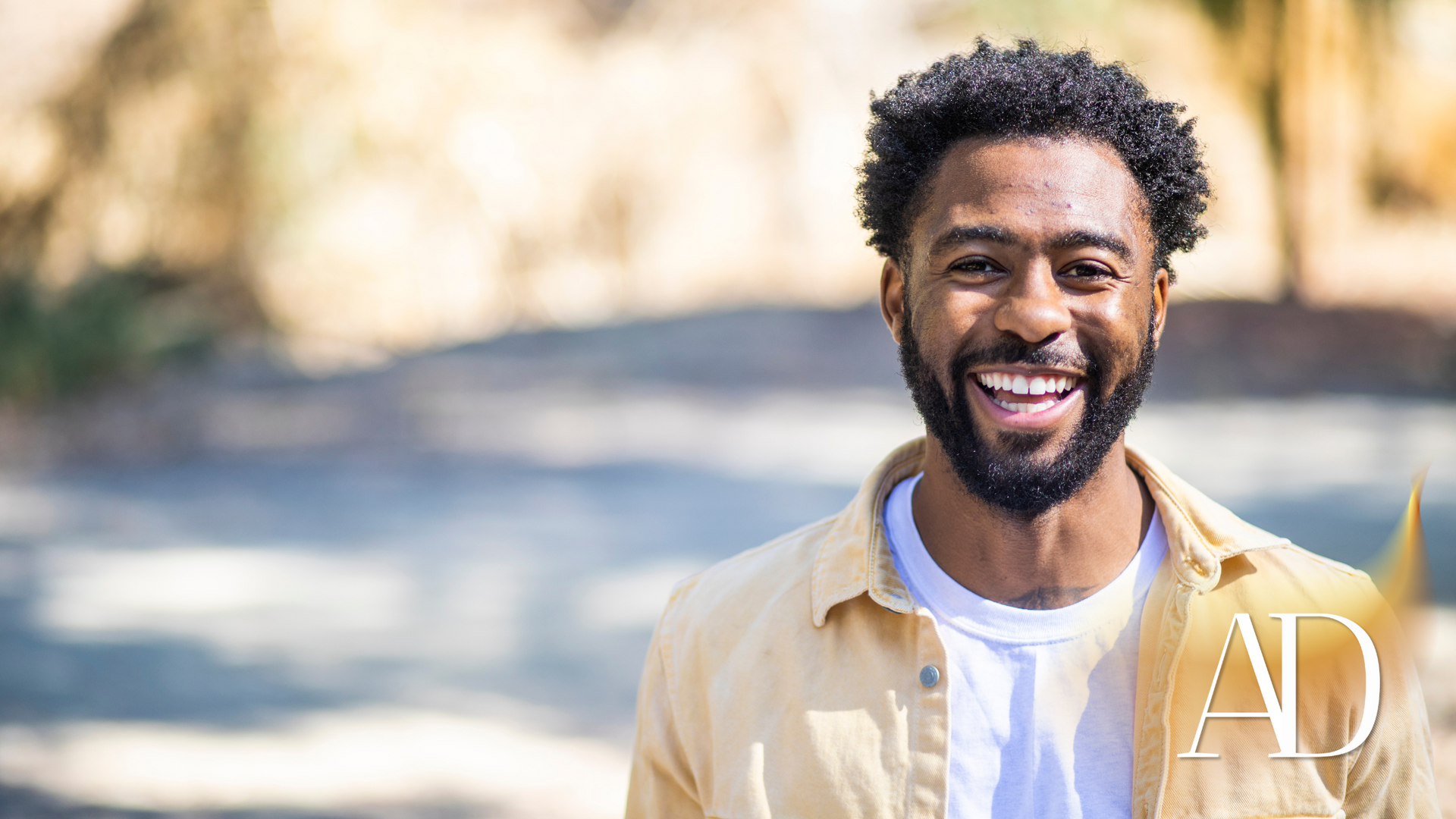 Smiling man outdoors in a beige shirt on a sunlit path