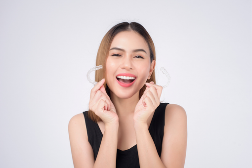 Smiling woman holding clear heart-shaped earrings against a light background