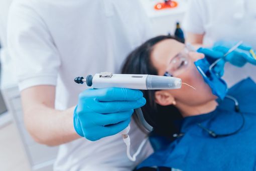 Dentist holding an electric toothbrush near a patient reclined in a dental chair during a dental exam