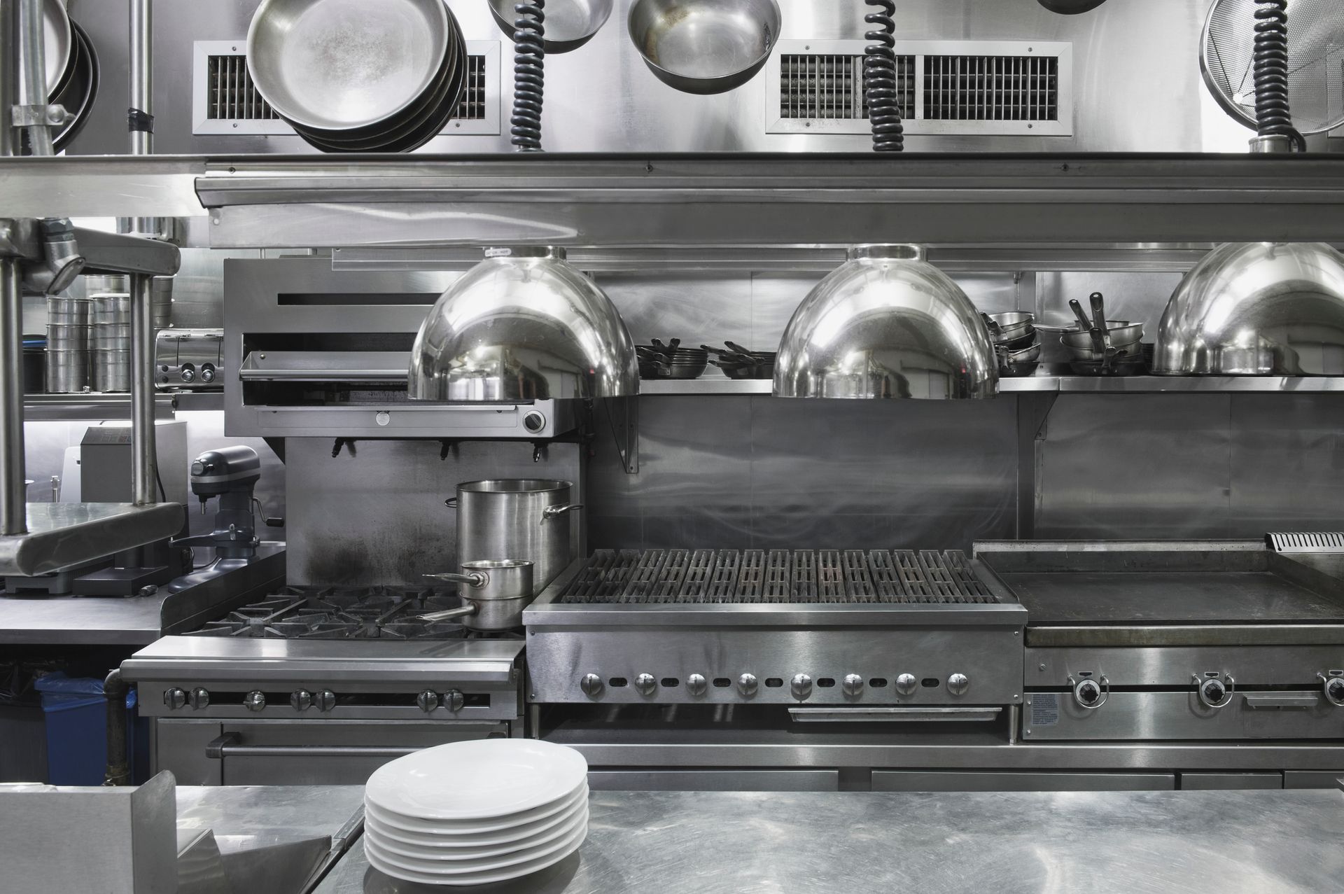 Commercial kitchen with stainless appliances, cookware, and plates.