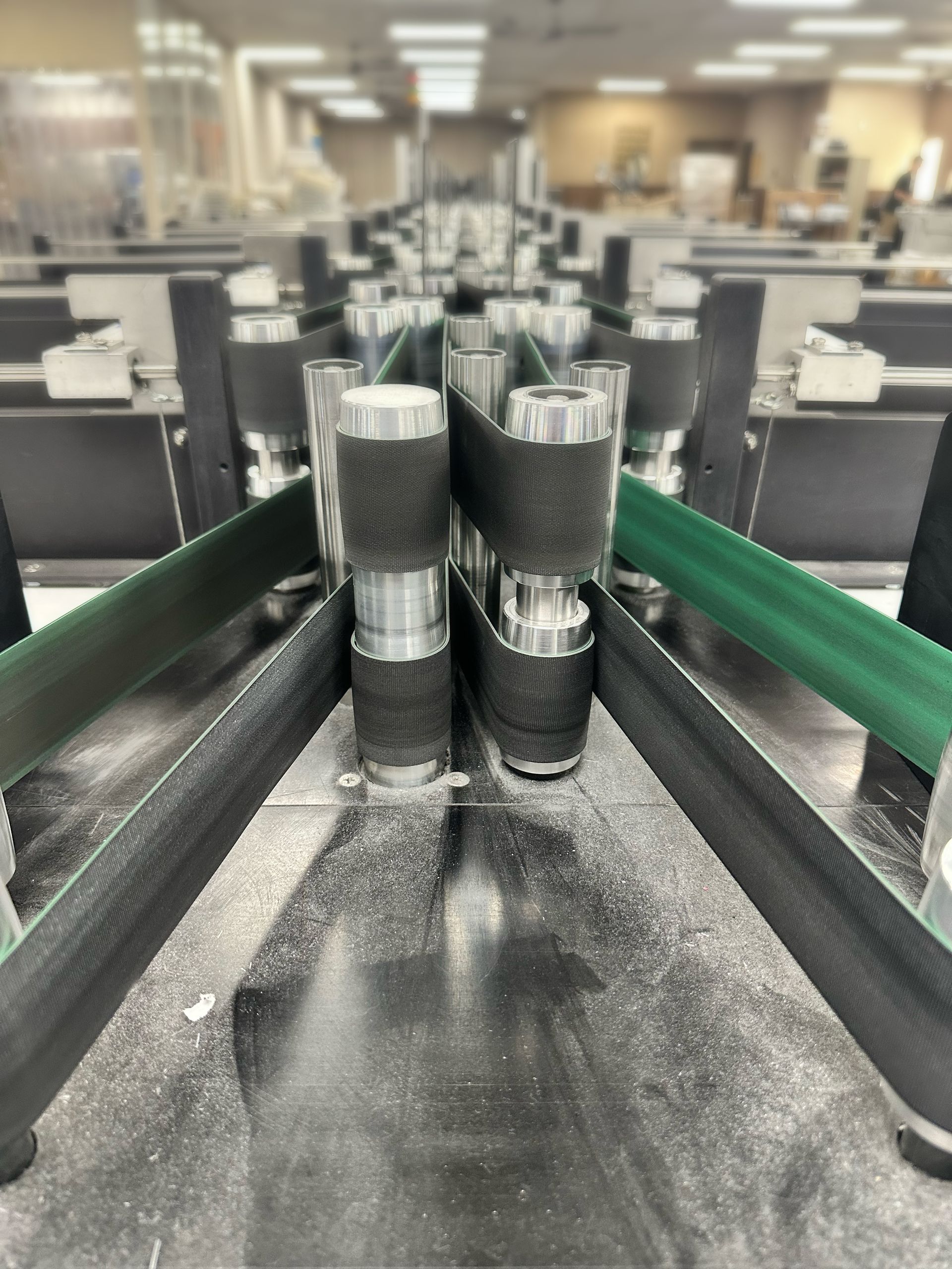 Two dark cylindrical parts on a black conveyor belt in an industrial factory assembly line.