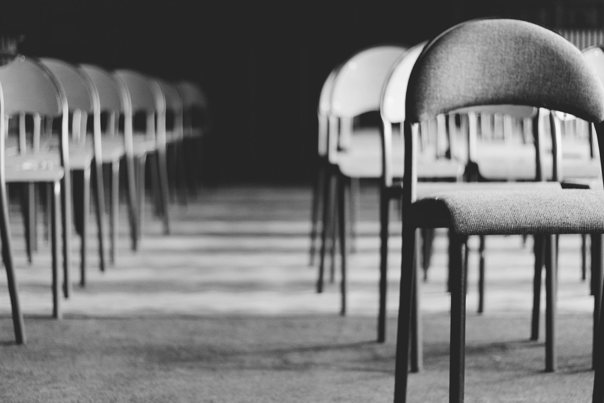 Rows of empty chairs in a black-and-white room, with one chair in the foreground