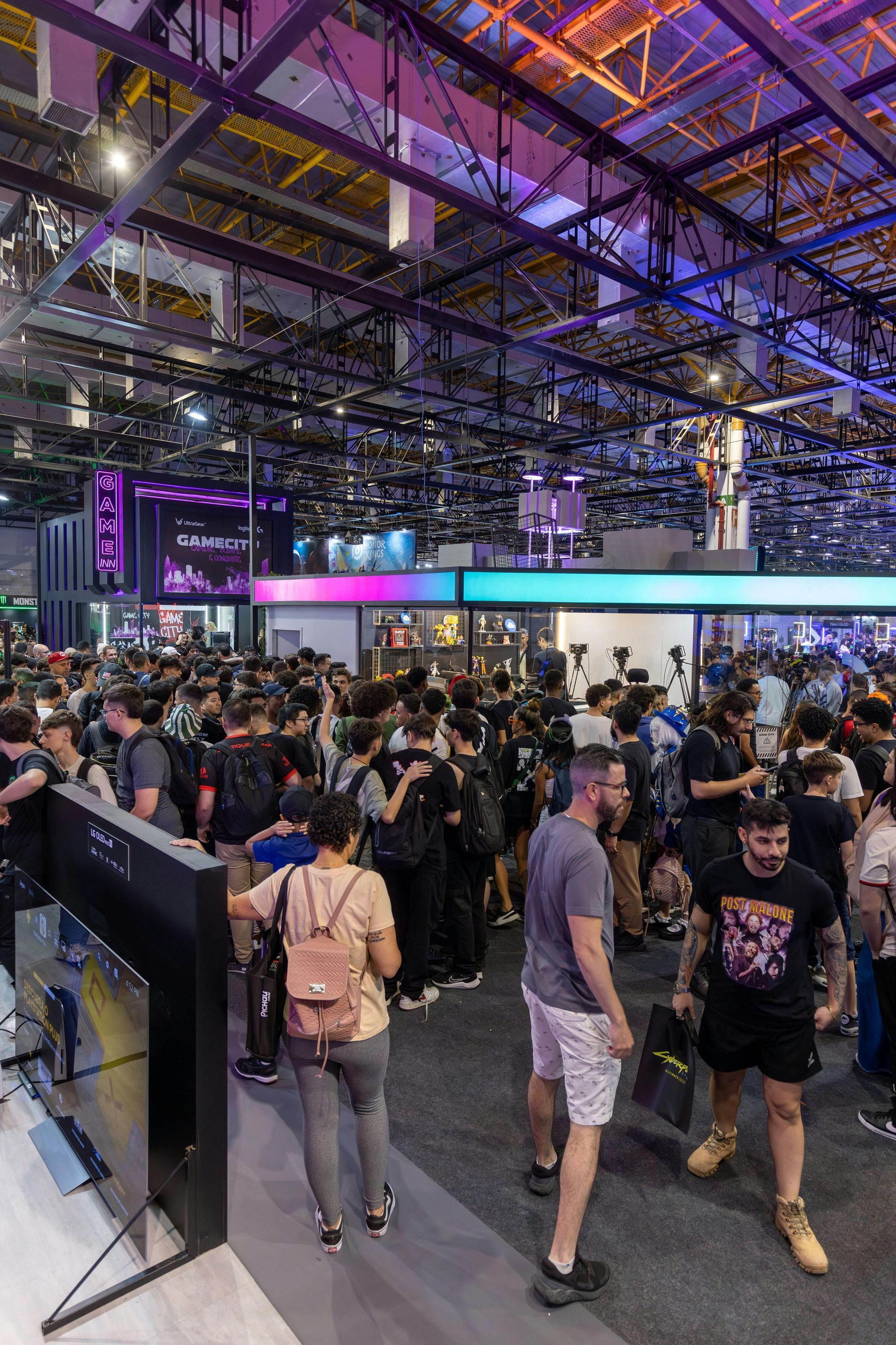 Crowded indoor expo hall with a large illuminated ceiling and people walking through booths