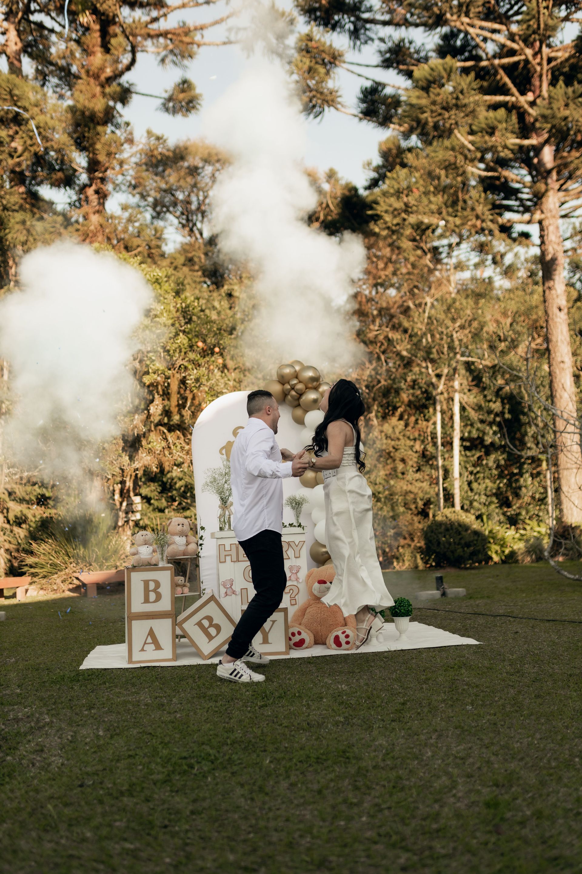 Outdoor wedding couple in white, embracing amid smoke and decorated wooden blocks on a lawn