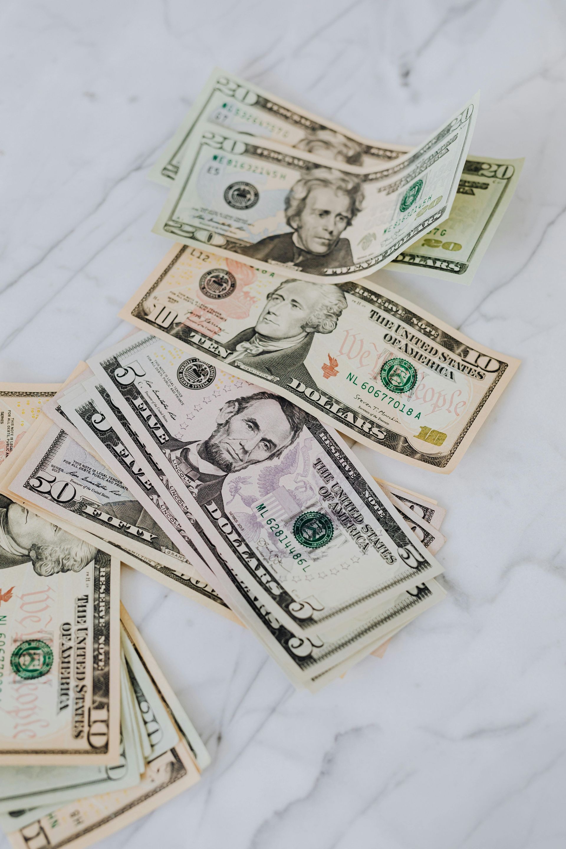 Scattered U.S. dollar bills on a white marble surface.