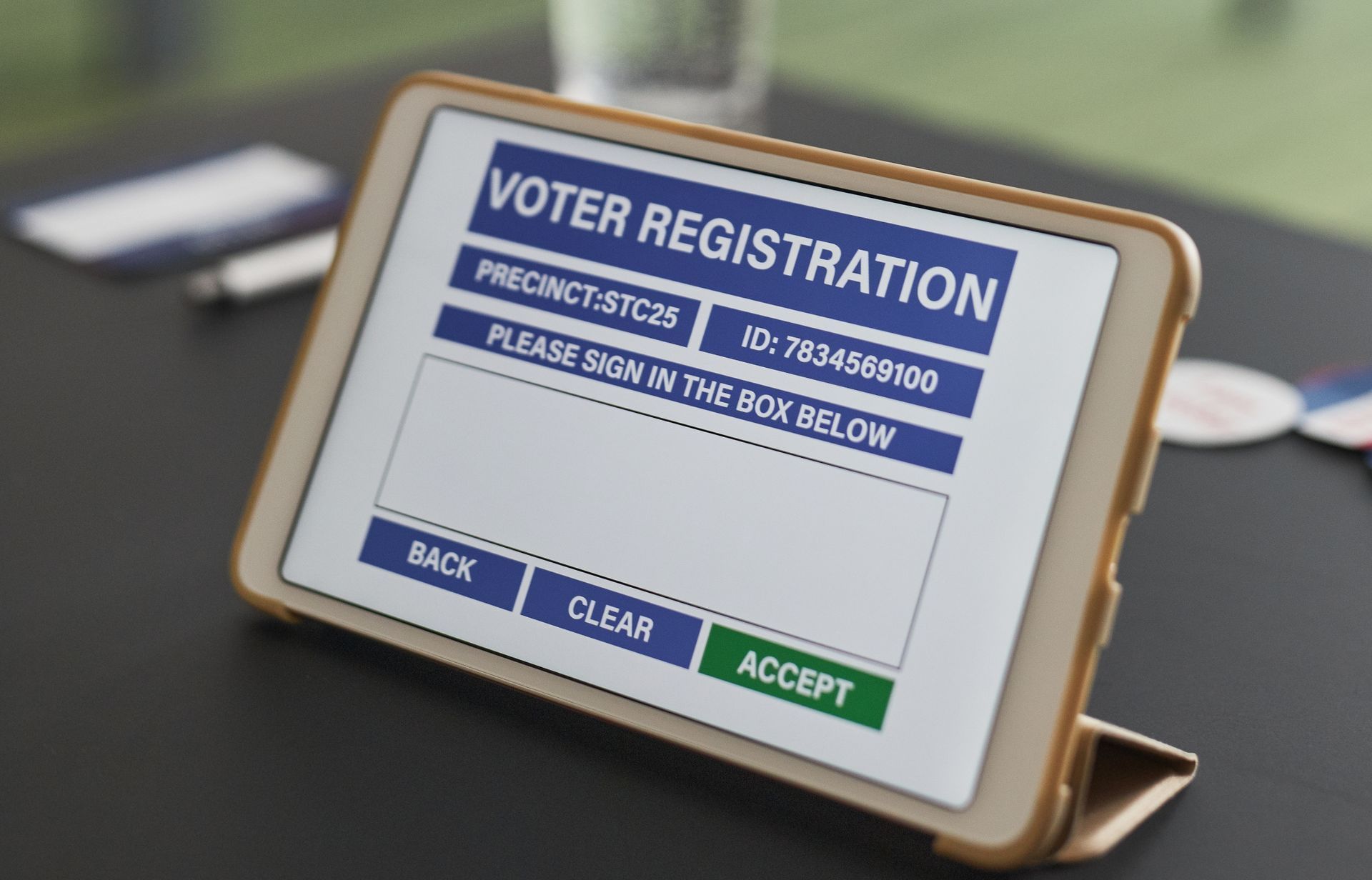 Tablet showing voter registration screen, with a blue header, signature box, and buttons.