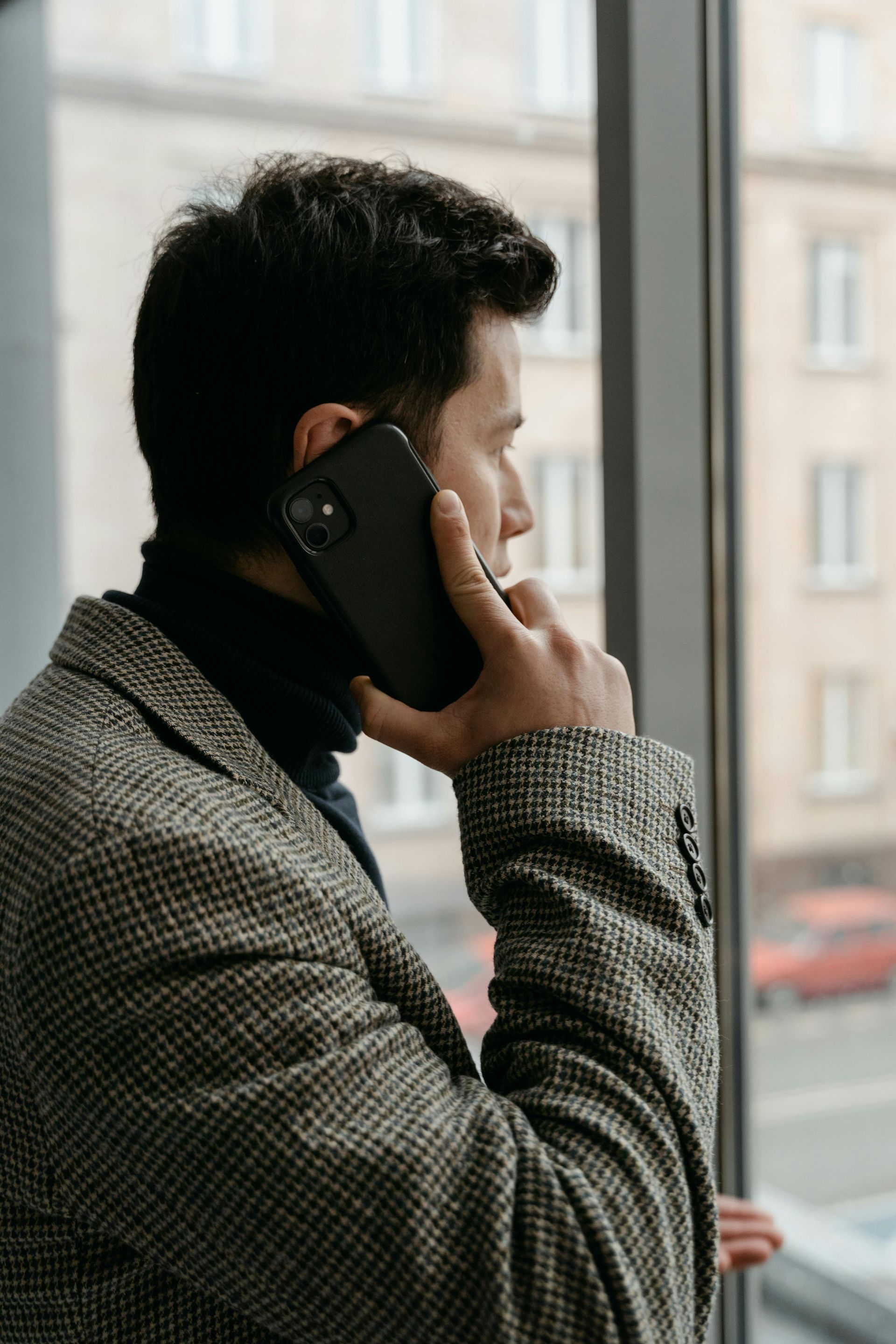 Person in a gray coat speaking on a phone by a window.