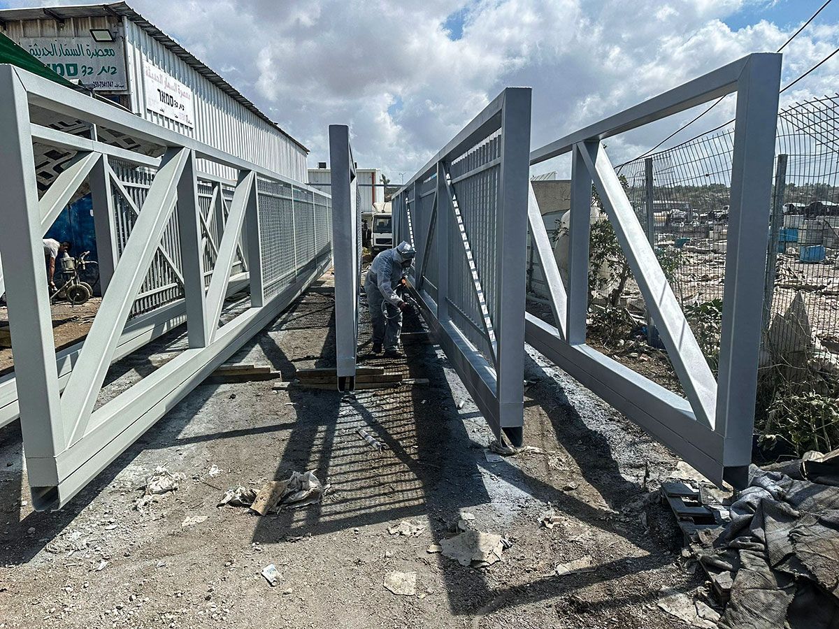 פועל מבצע עבודות הרכבה והכנה על קונסטרוקציית מתכת מסיבית, כחלק מתהליך ייצור של שערים חשמליים כבדים וקלים.