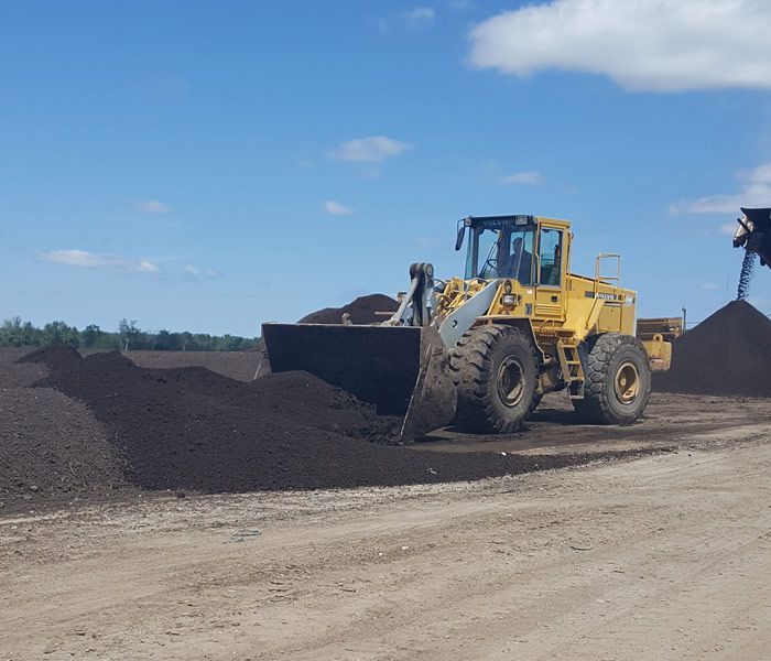 Yellow front loader pushing black gravel at a construction site under a blue sky.