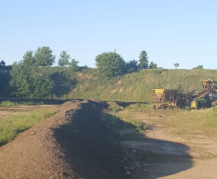 Construction equipment on a dirt road at a gravel quarry under a clear blue sky.