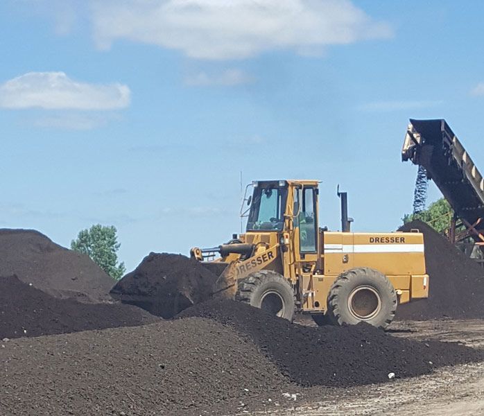 Yellow construction loader moving dark gravel in a quarry under a blue sky