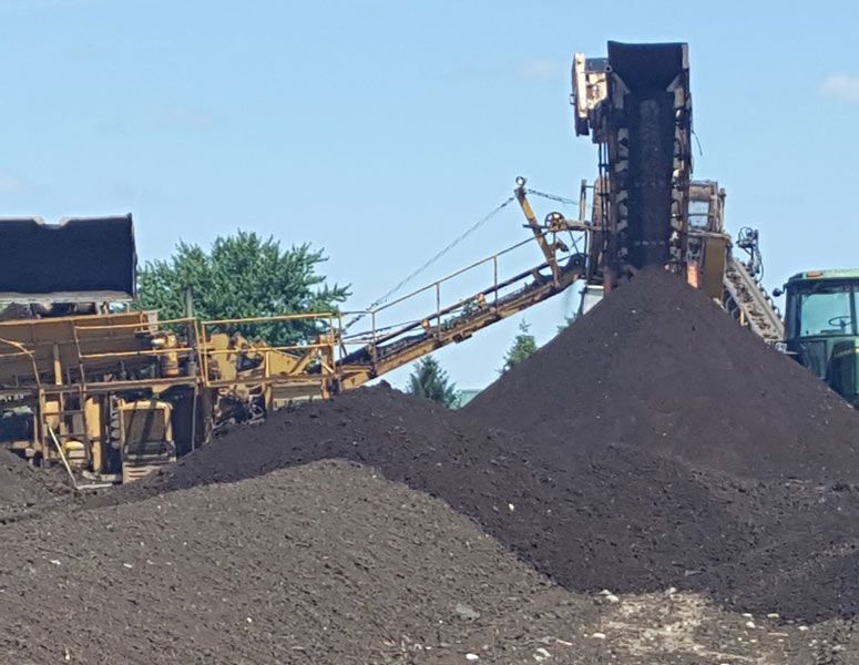 Industrial machinery with a conveyor piling dark gravel under a clear blue sky