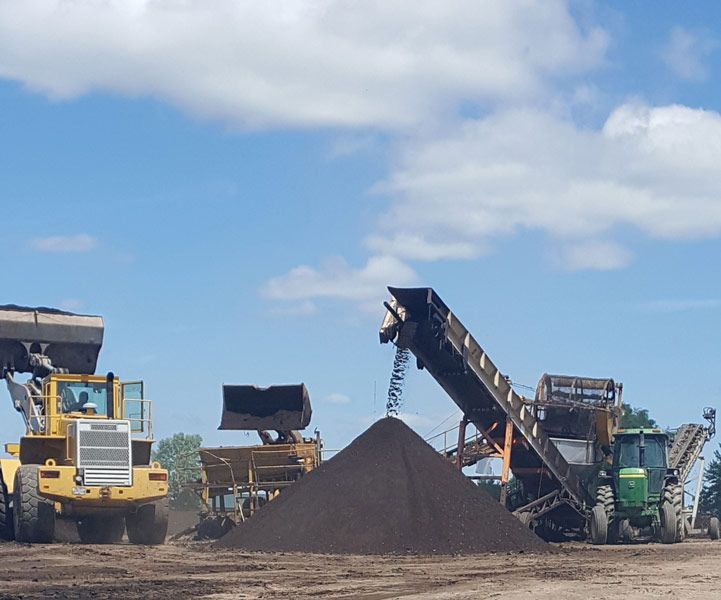 Construction equipment piling dark gravel at an open work site under a blue sky