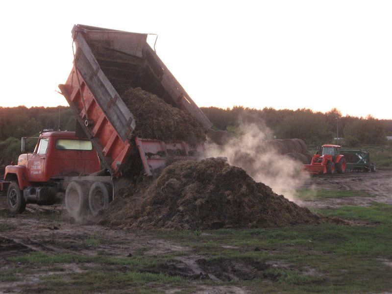 Red dump truck unloading a large pile of dirt at a worksite at dusk