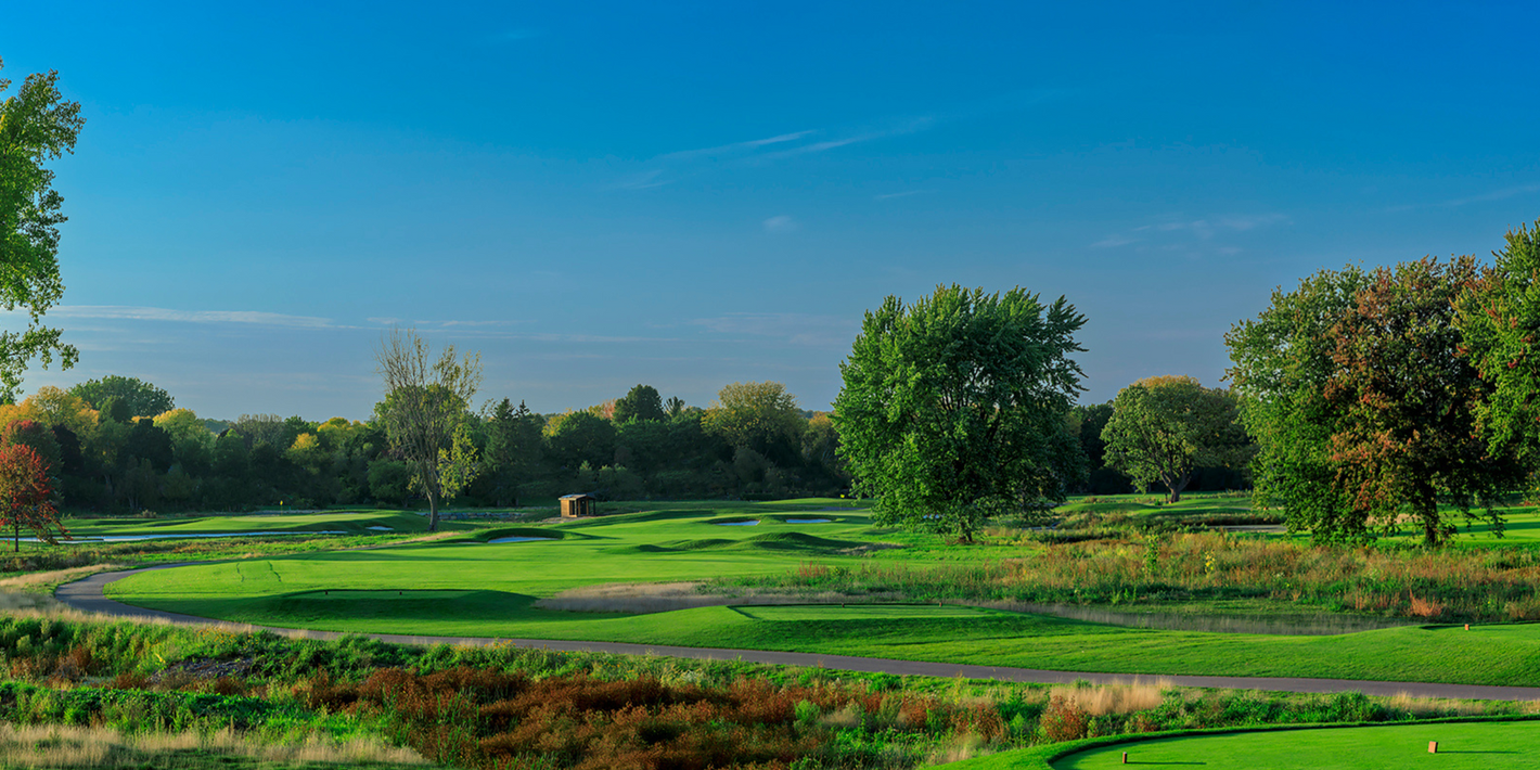 A golf course with a lot of green grass and trees on a sunny day.