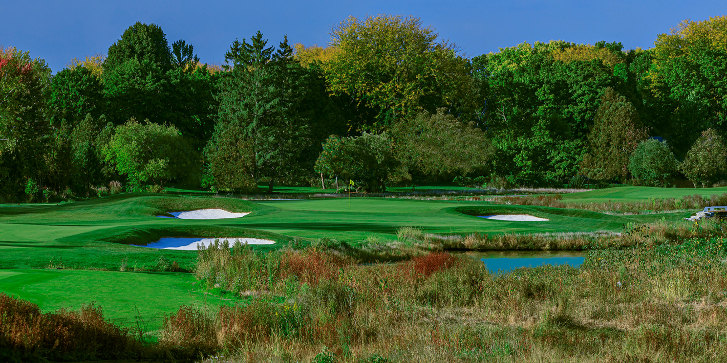 A golf course surrounded by trees and grass with a pond in the middle.