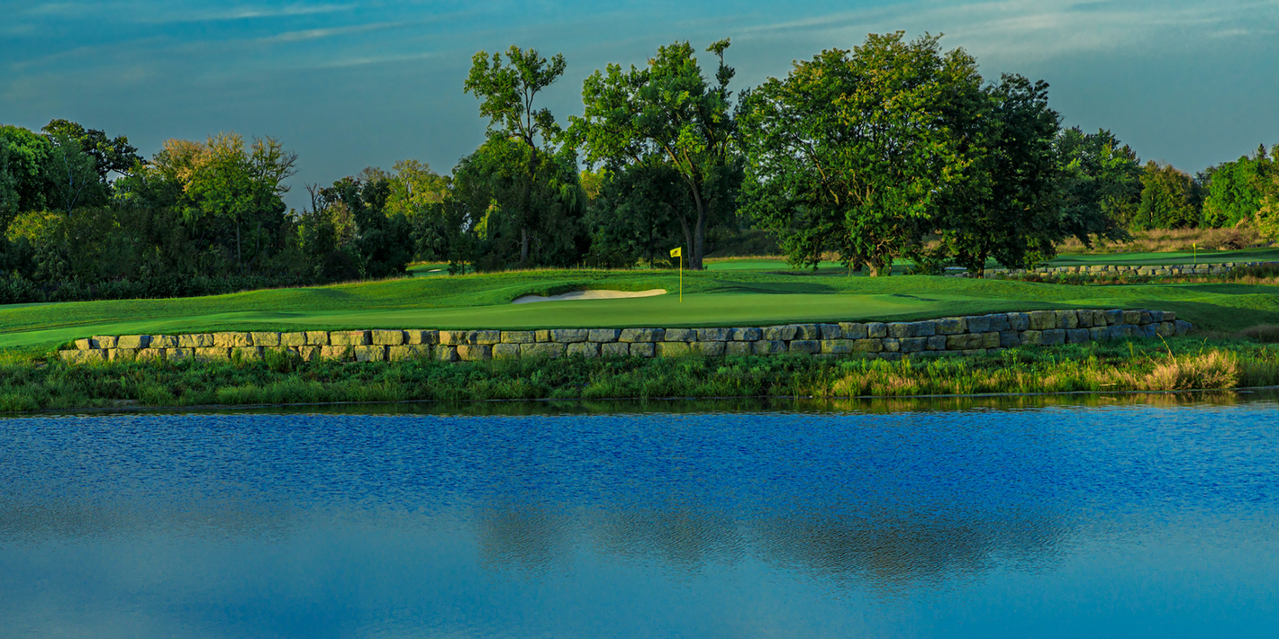 A golf course with a lake in the foreground and trees in the background.