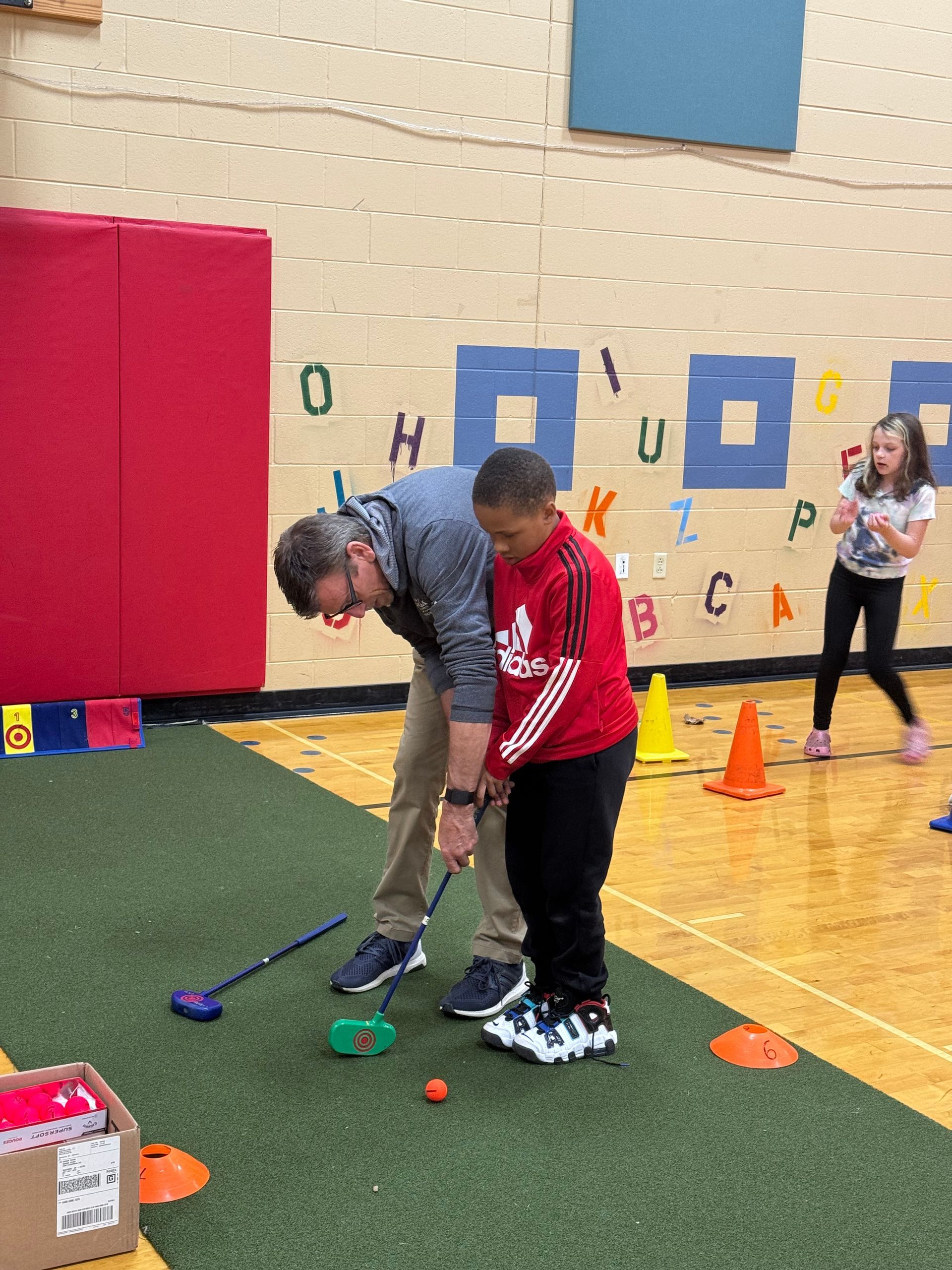 A man is helping a young boy play golf in a gym.