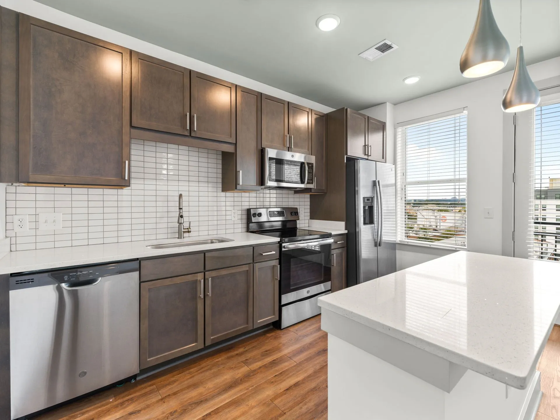 Modern kitchen with dark wood cabinets, stainless steel appliances, white island, and wood flooring.