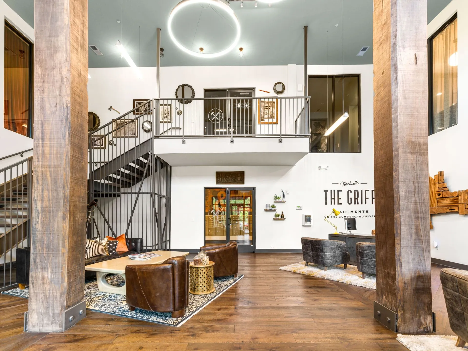Bright lobby with a spiral staircase, large pillars, wooden floors, and modern seating under circular ceiling lights