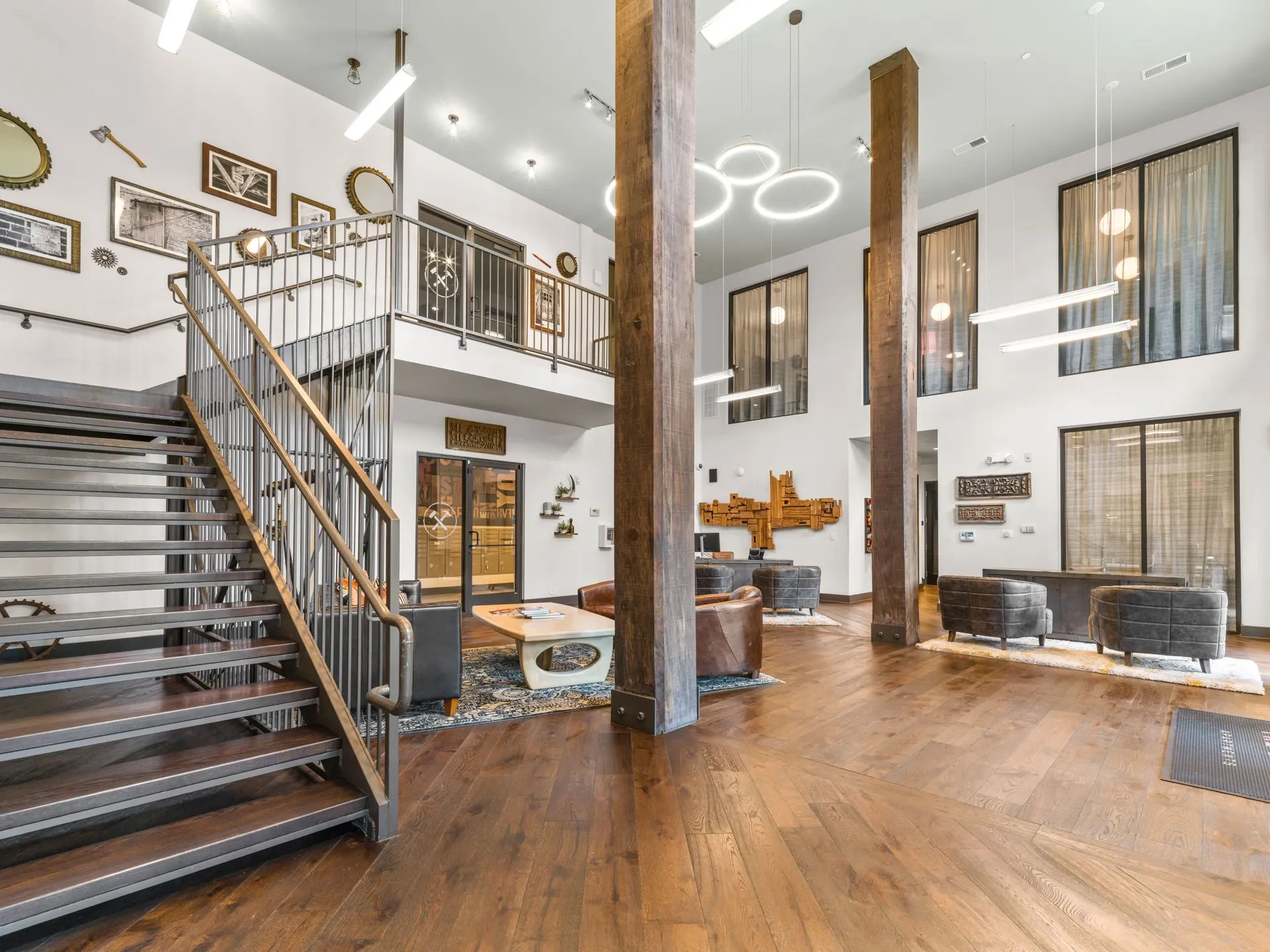 Modern two-story lobby with staircase, wood floors, white walls, and circular pendant lights